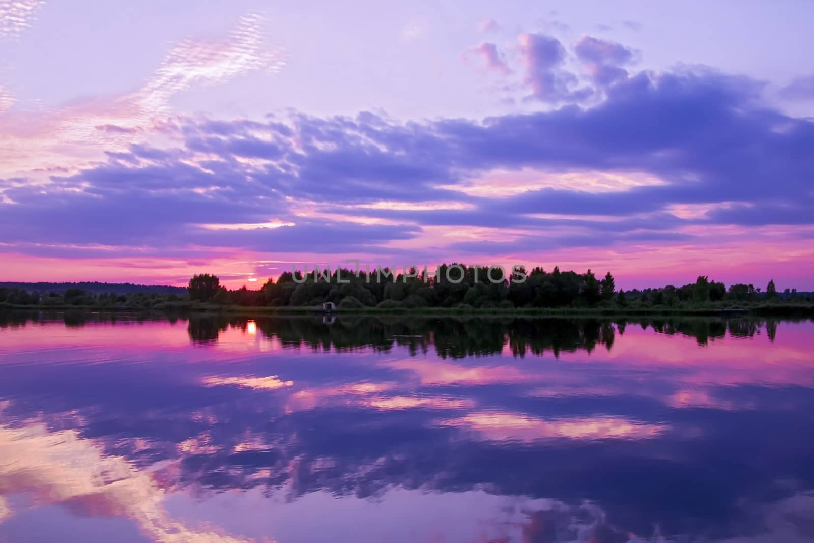 Panorama reflection of sunset in the water of the lake. The sky and clouds, illuminated by the sun setting over the horizon, acquired unusual purple and lilac colors.