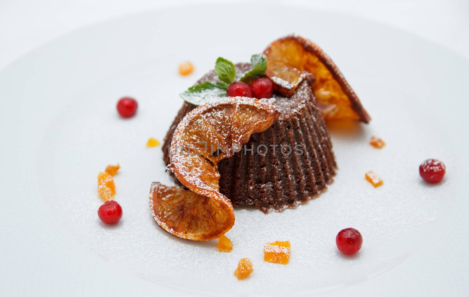 Chocolate orange cupcake decorated with fresh berries, sliced orange, mint on white plate