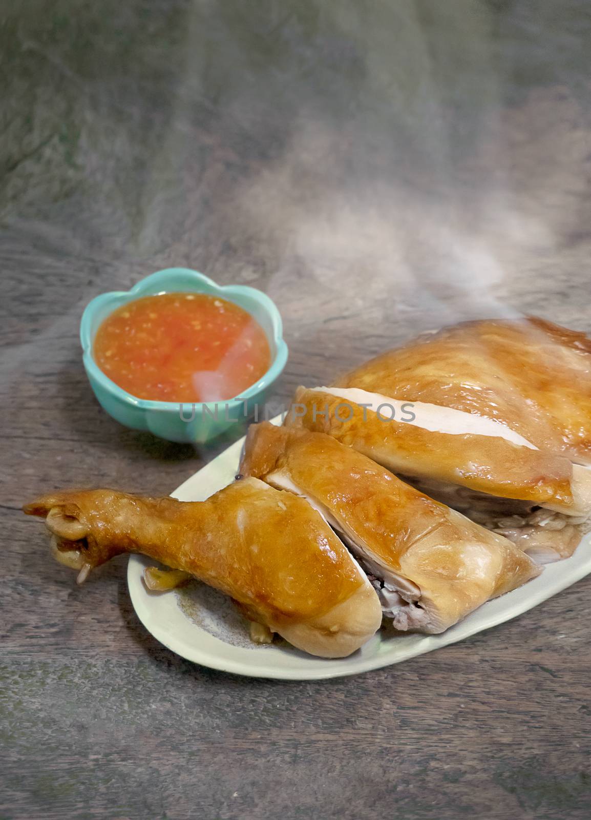 Steamed chicken with soy sauce on dish served with chili sauce in green bowl , Asian style food