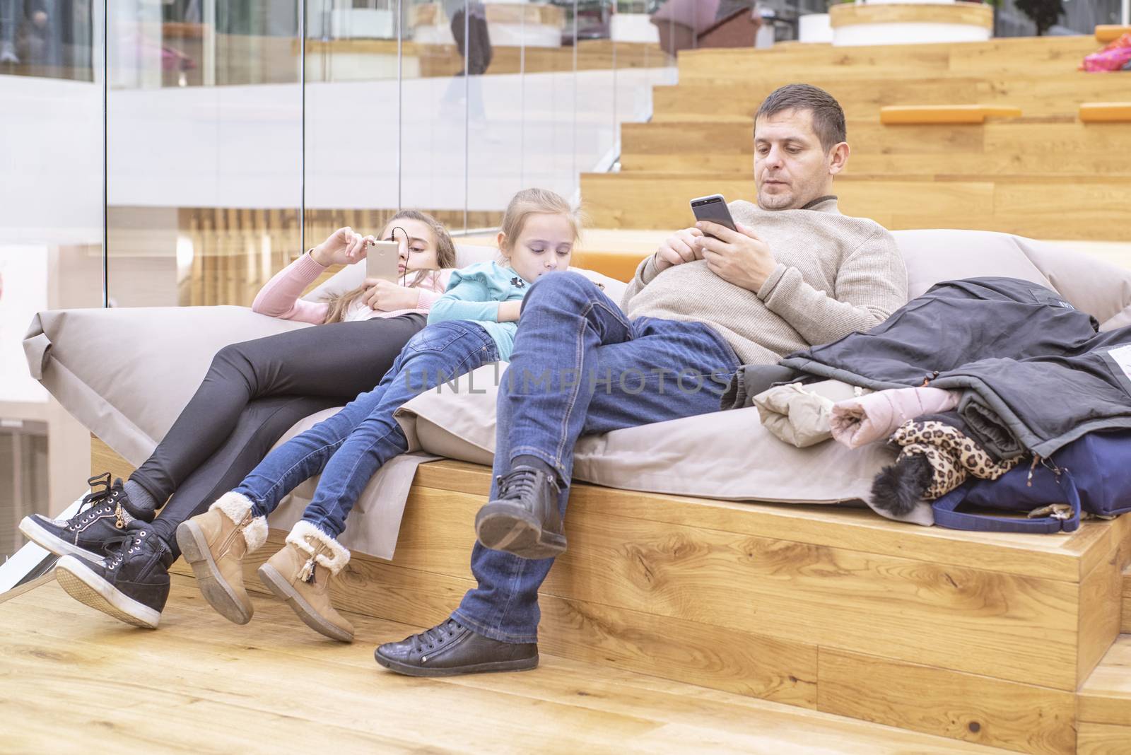 The father is resting with the kids in the store.Father with children is waiting on the easy chairs in the store.