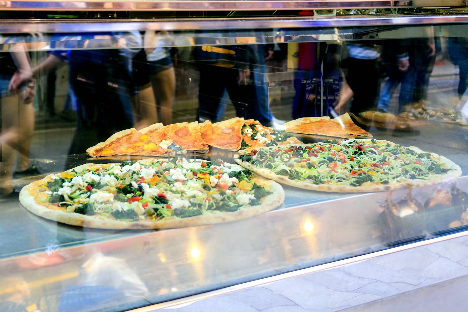 A pizzeria showcase with real Italian pizza and silhouettes of passing people in, reflected in the showcase. Venice, Italy,