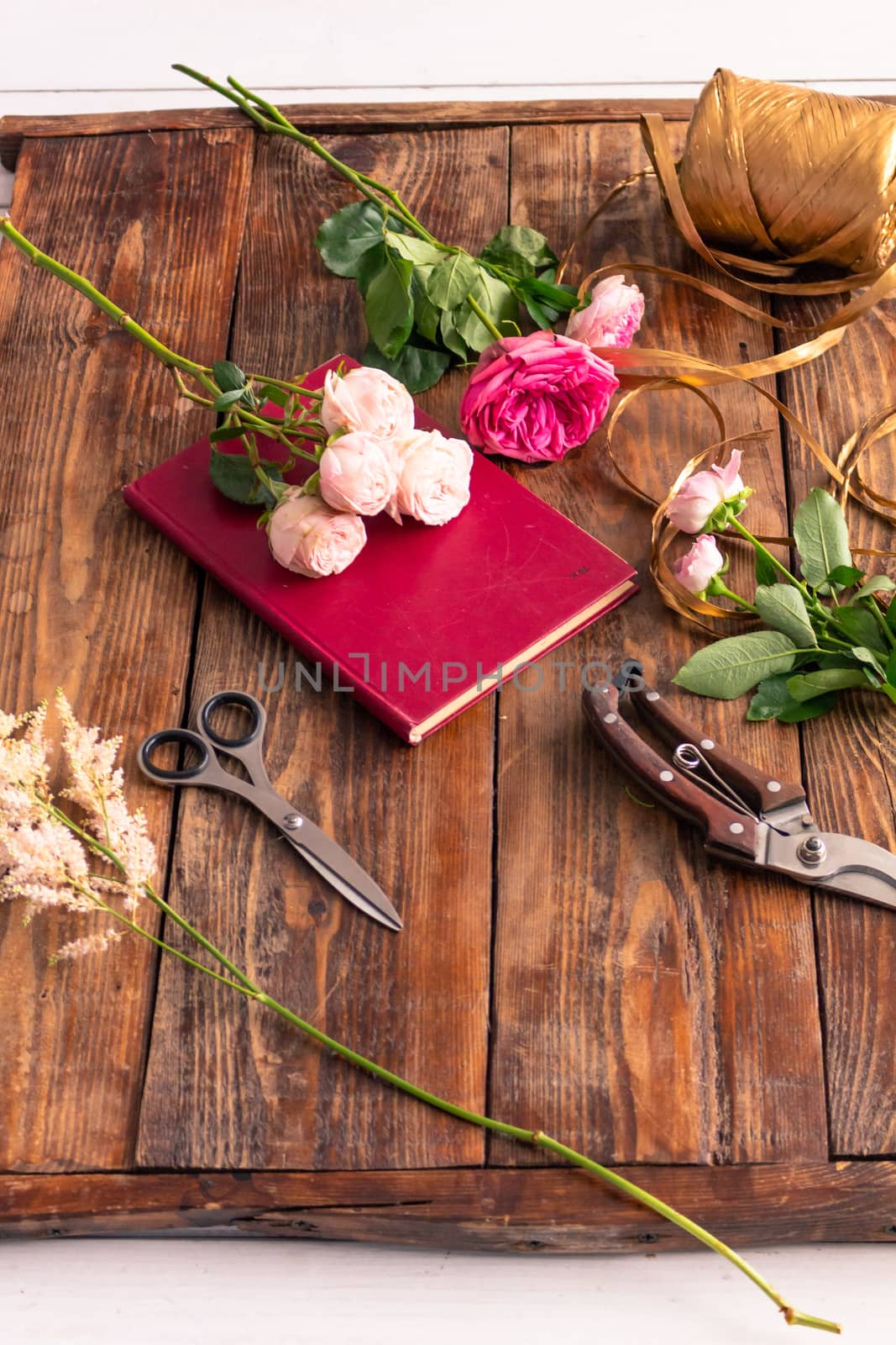 On the wooden surface laid out tools for flower bouquets: scissors, roses, colored ribbon, roses.