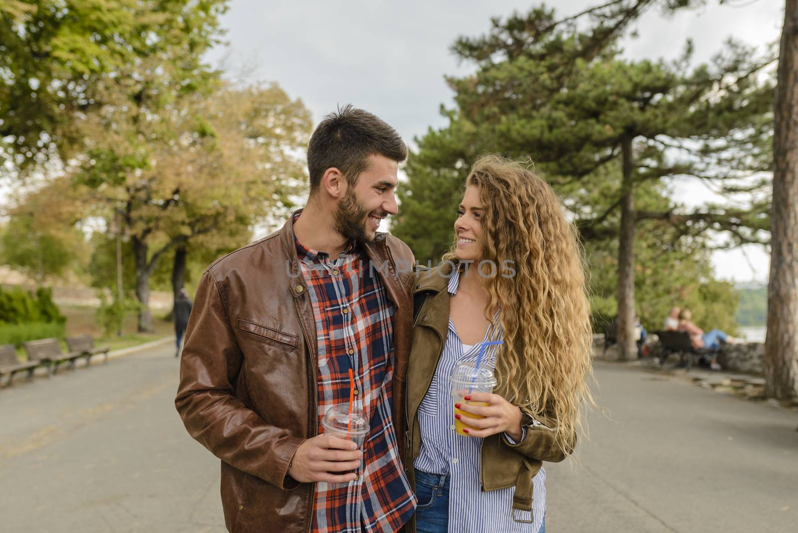 Attractive couple is refreshing with juice in the public park while smiling at each other