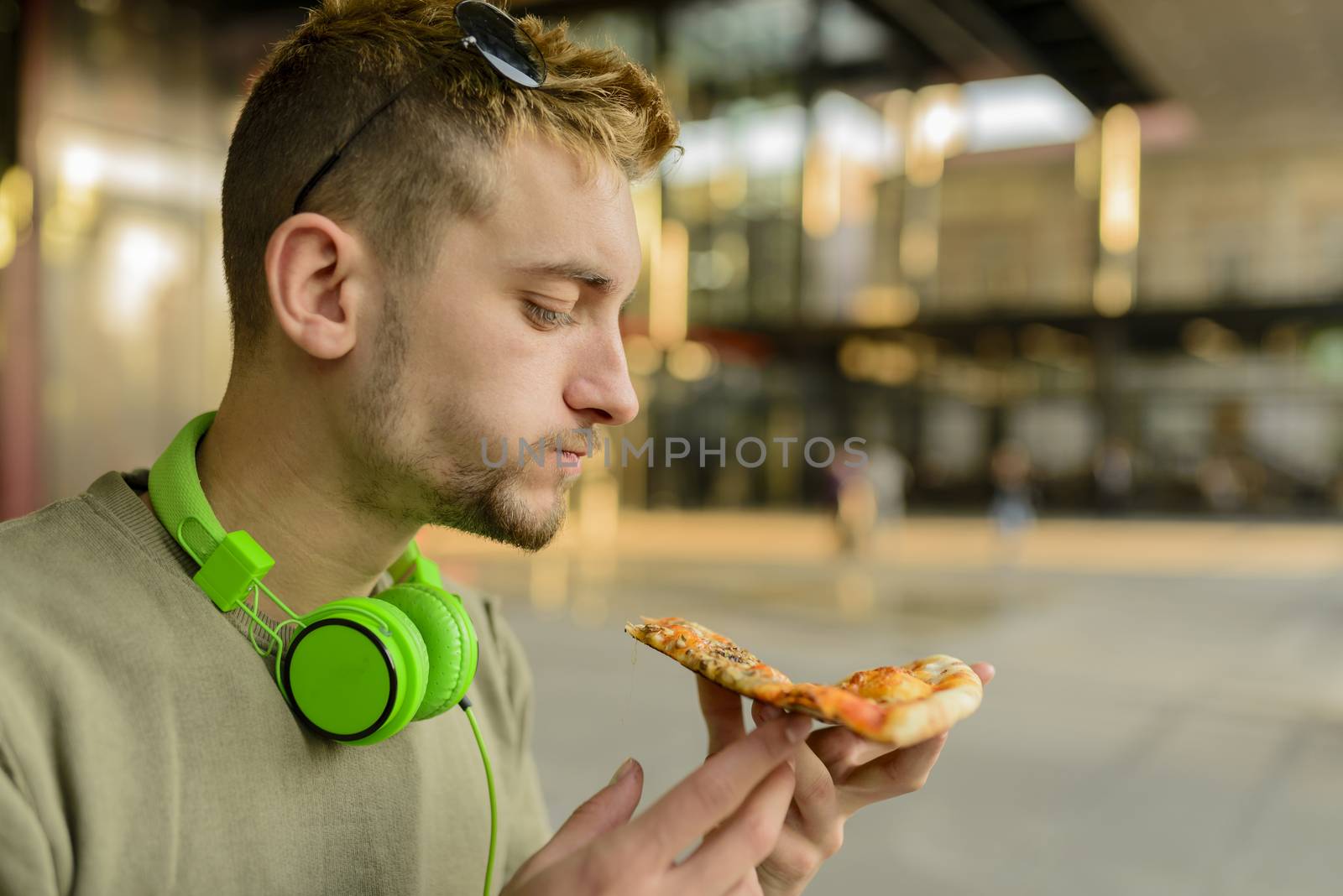 Handsome young man with headphones eating pizza in the city street