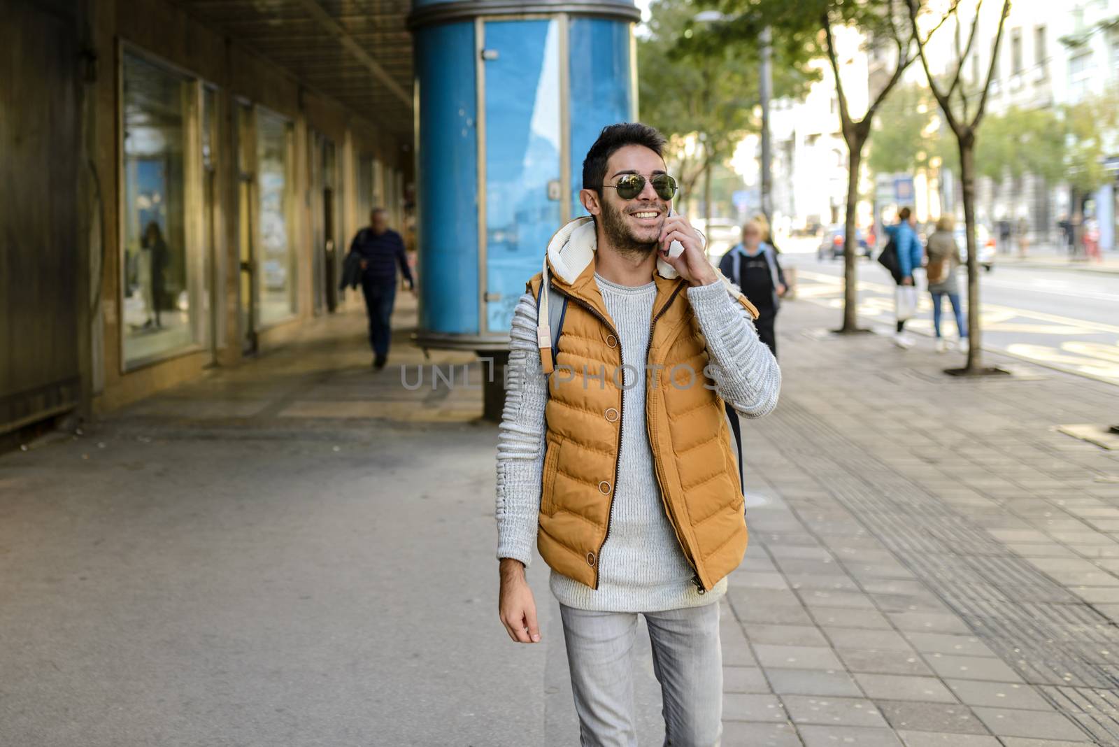 Young hipster with orange jacket and sunglasses with his smart phone in the city street