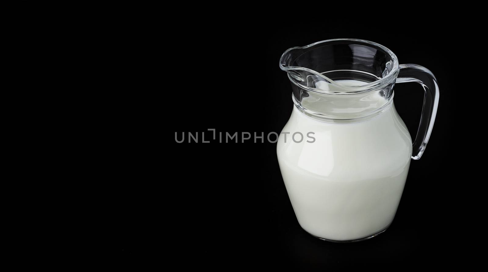 Glass jug of fresh milk on black background with copy space, pitcher of cream