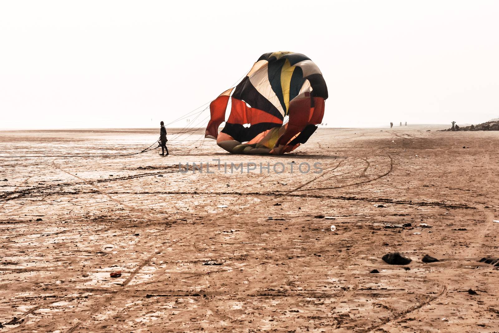 Skydiver with orange and yellow parachute runs after landing in Dona Paula Beach, near Colva and Vagator Beach Goa against sky and sea water. Paragliding parachuting is an extreme sport of recreation. by sudiptabhowmick