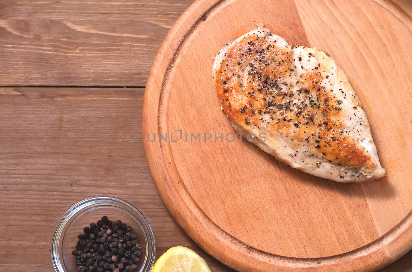 Grilled chicken fillet cooked in spices, sprinkled with salt and pepper, next to spices and lemon