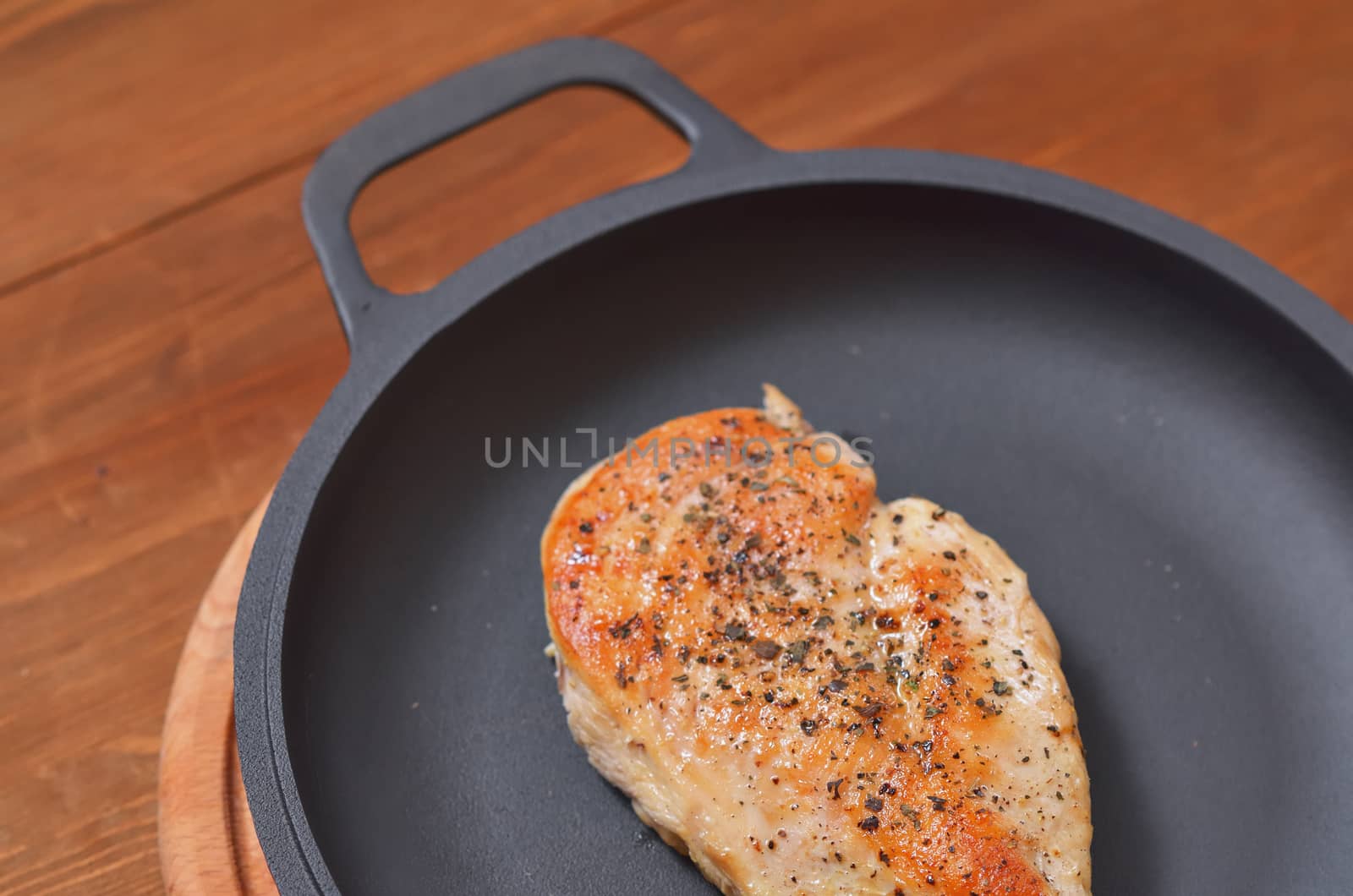 Fried chicken fillet is lying on a frying pan on a wooden table