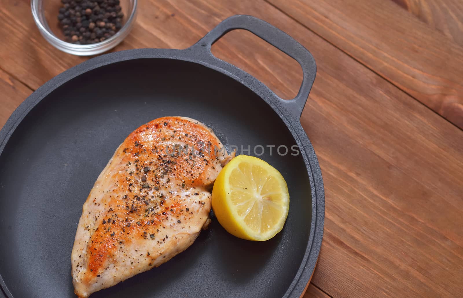 Fried chicken fillet grilled in a frying pan with lemon and spices on a wooden table