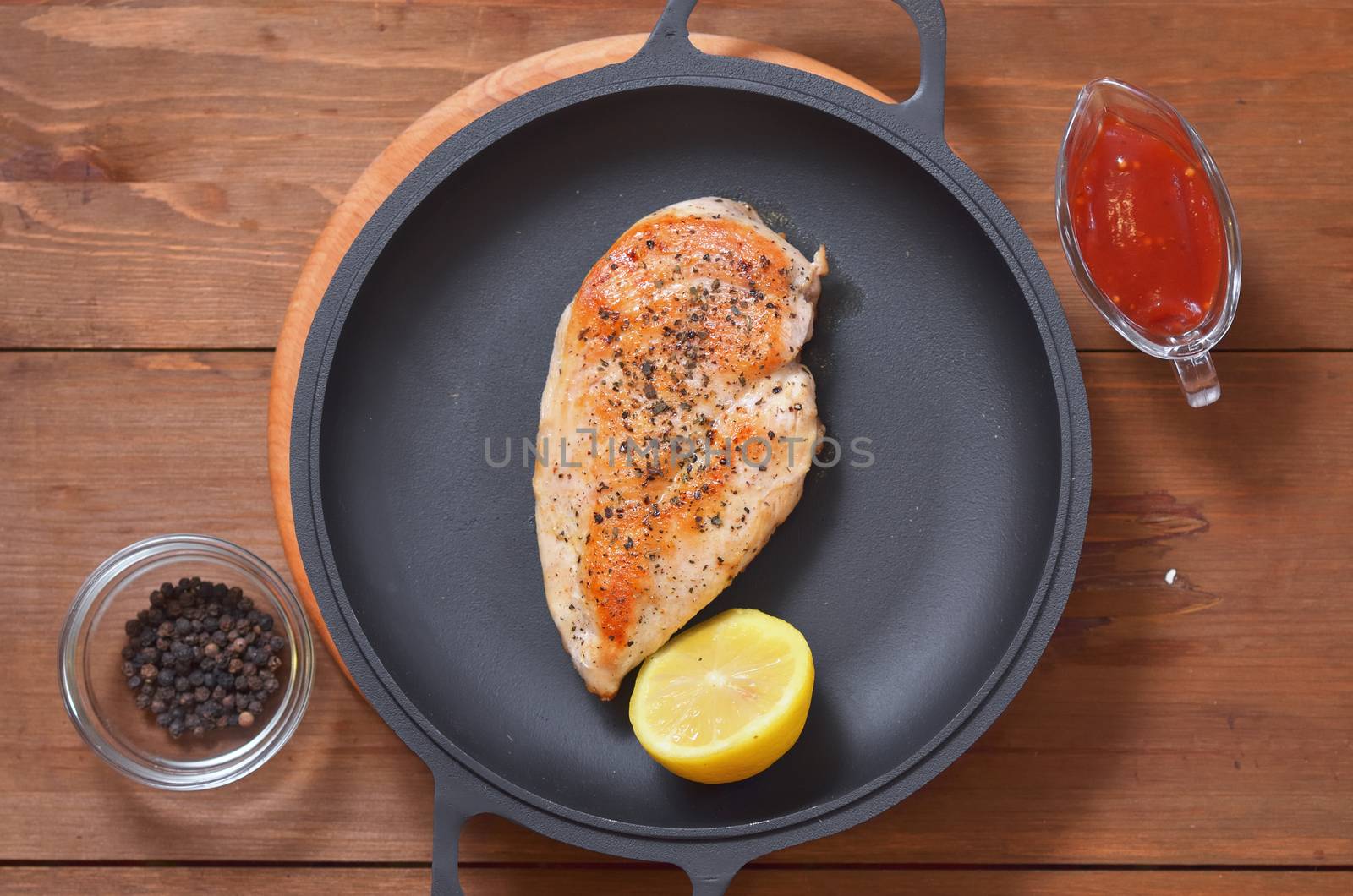 Fried chicken breast with lemon in a pan, spices and a sauce on a wooden table
