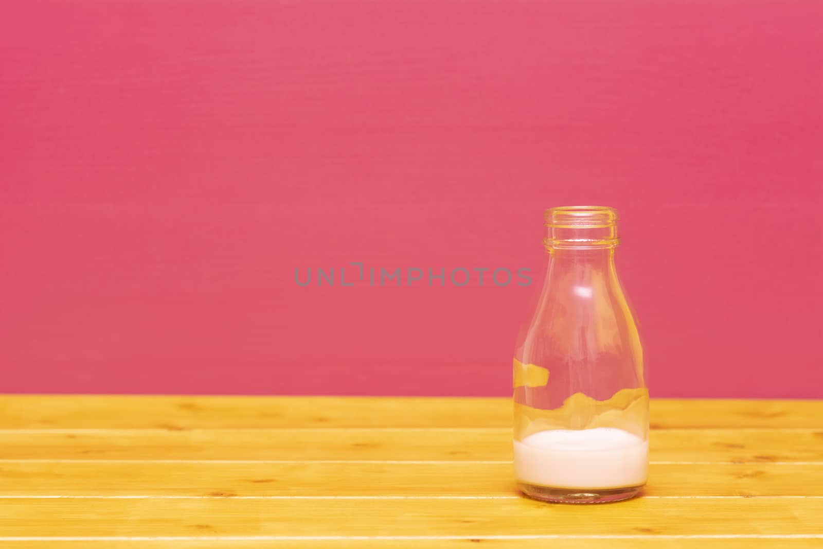 One-third pint glass milk bottle with dregs of strawberry milkshake, on a wooden table against a pink painted background