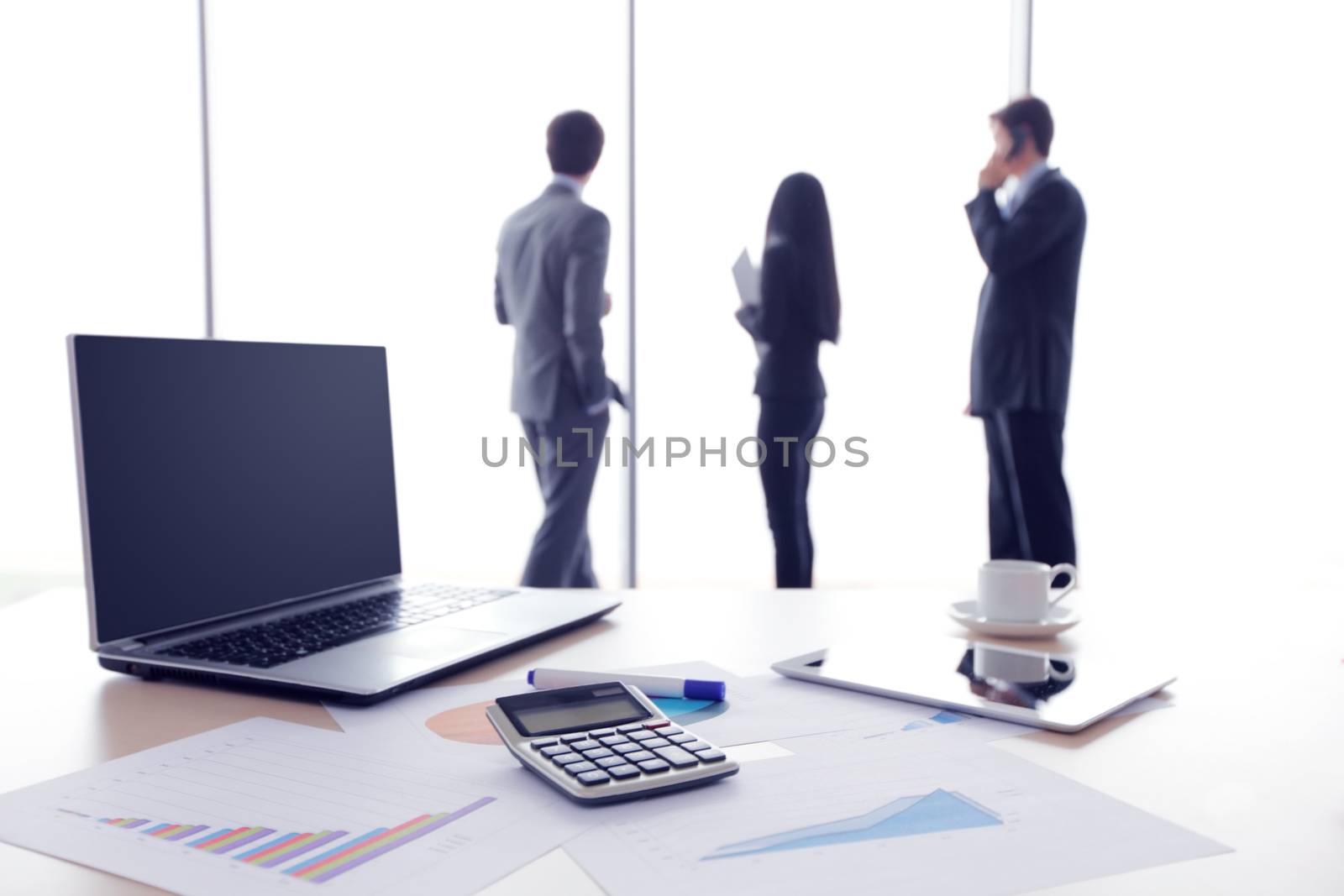 Financial documents , laptop, calculator on table , business team on background