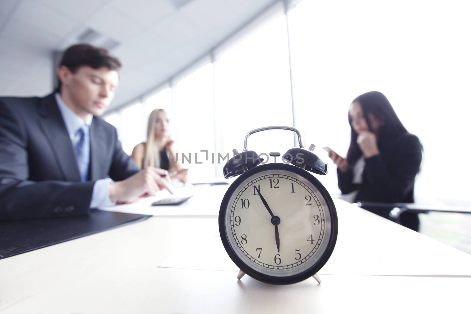 Alarm clock on office table with business discussion people group or meeting team background