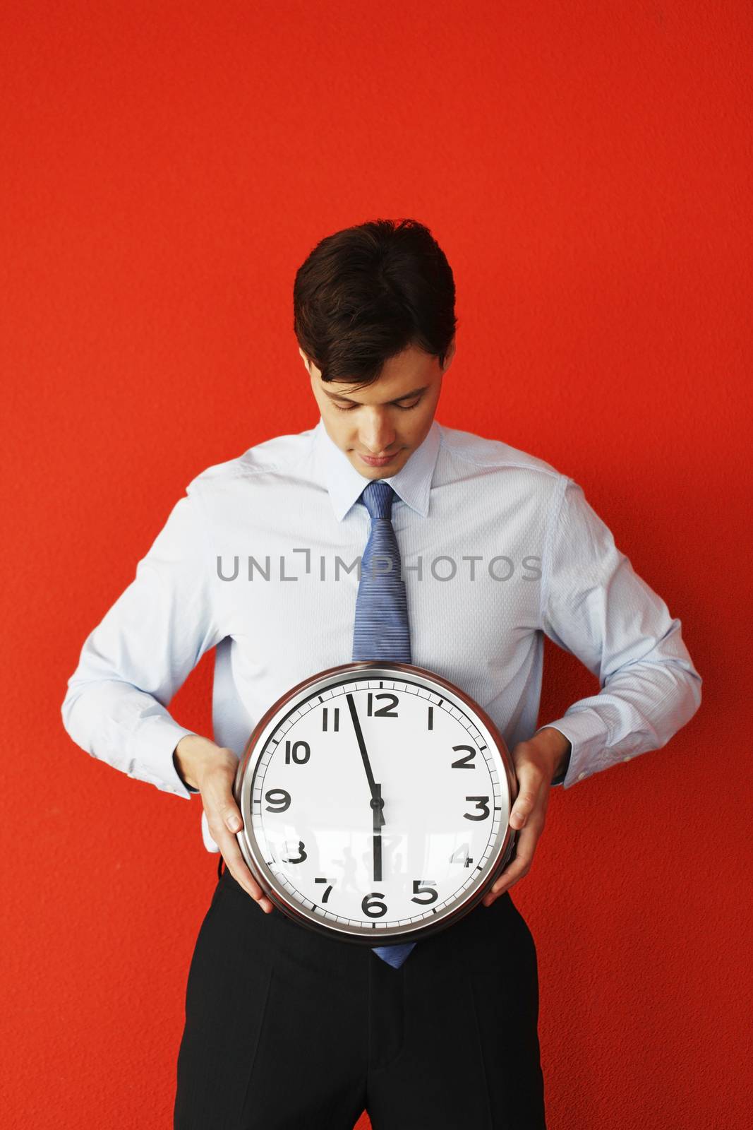 Business man holding wall clock on red background. Race against time, time goes by, running out of time, no time for work, time running, time is money concept