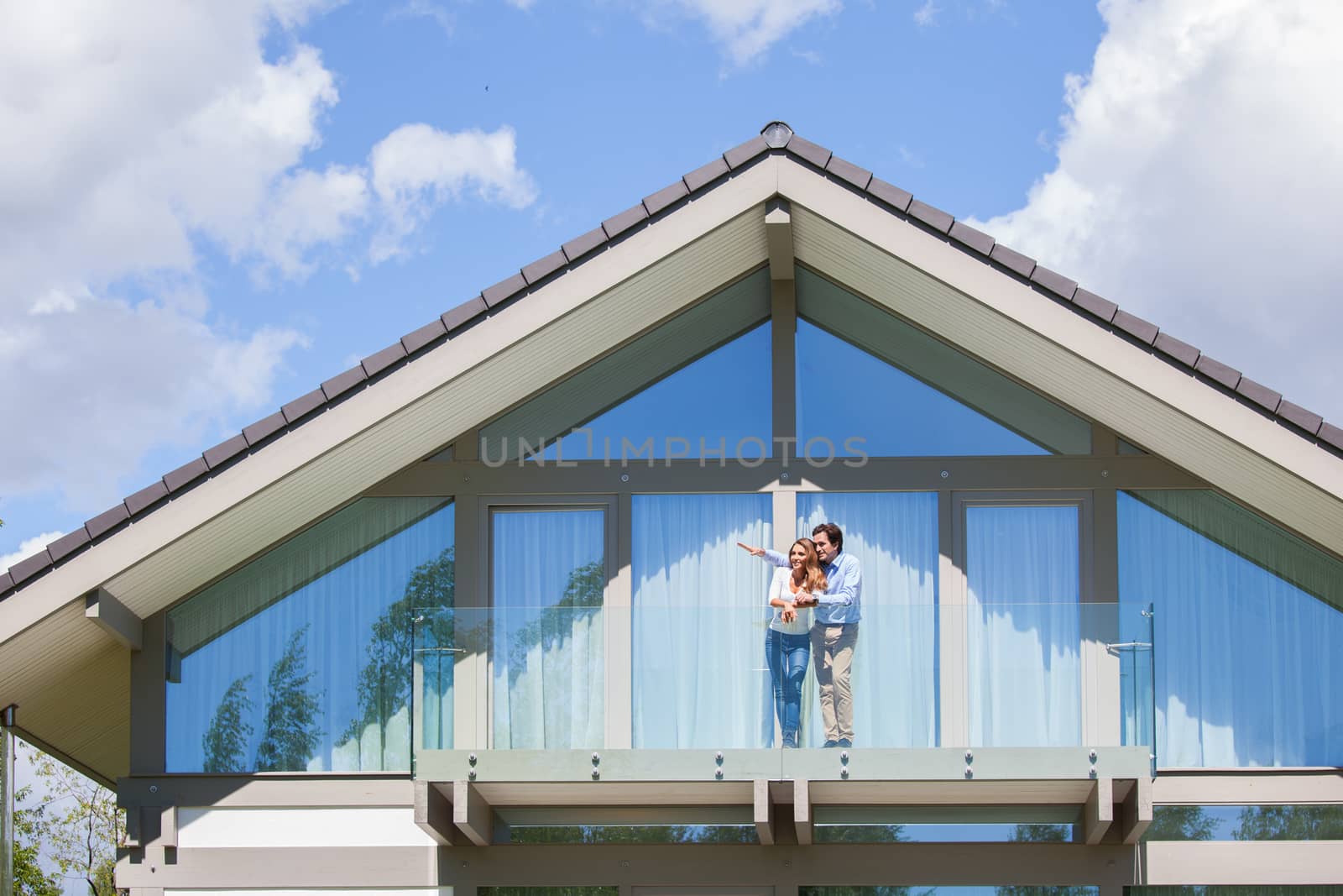 Happy couple standing on the balcony of their house and waving hands