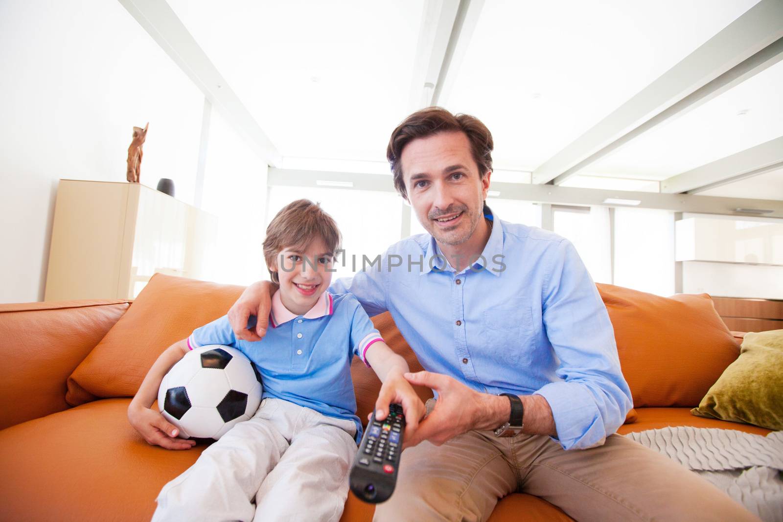 Portrait of happy boy watching soccer match with father on sofa at home