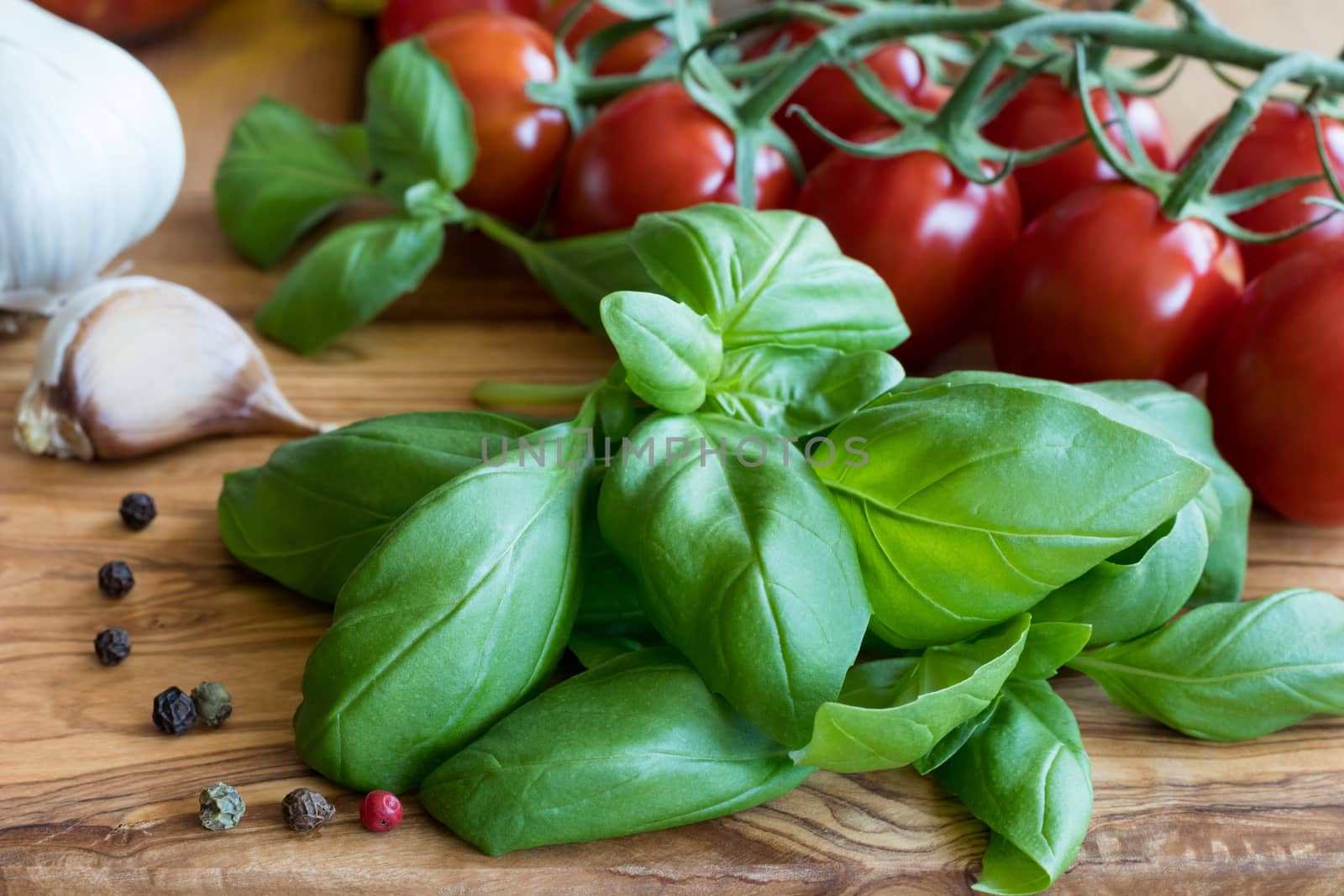 Fresh ingredients for Italian cuisine - basil, cherry tomatos, garlic and pepper on a wooden table