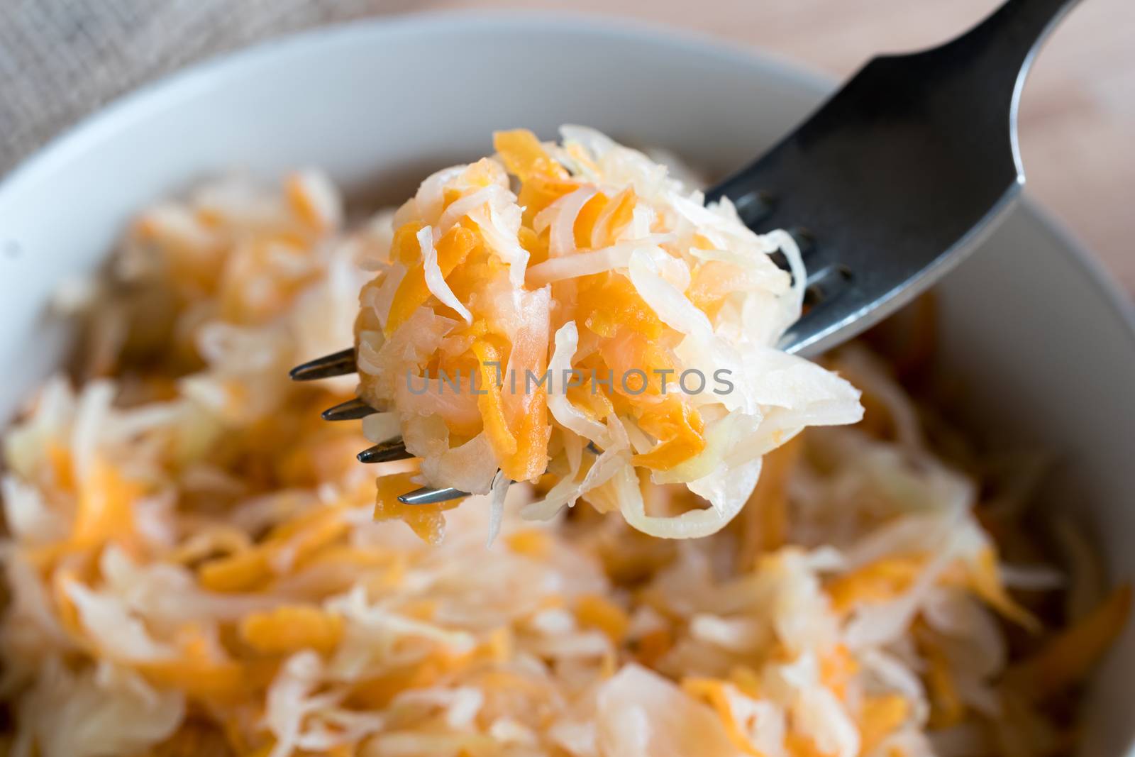 Fermented cabbage and carrots on a fork above a bowl of fermented vegetables