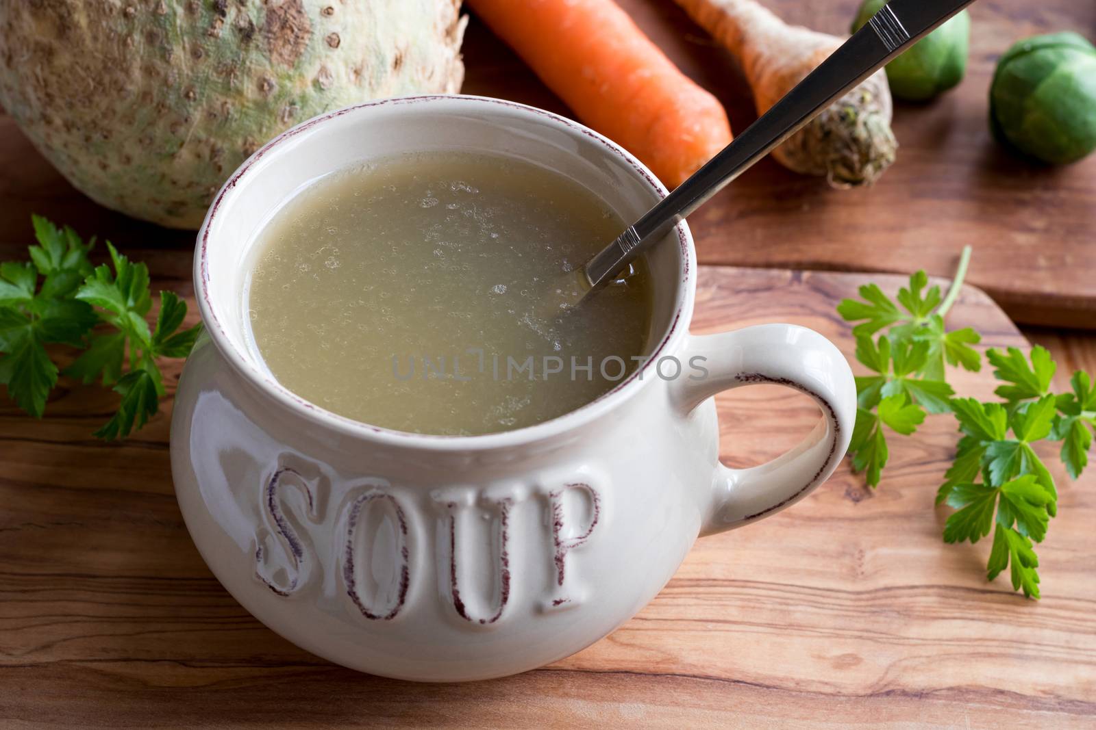 Bone broth made from chicken in a soup bowl on a wooden table, with vegetables in the background