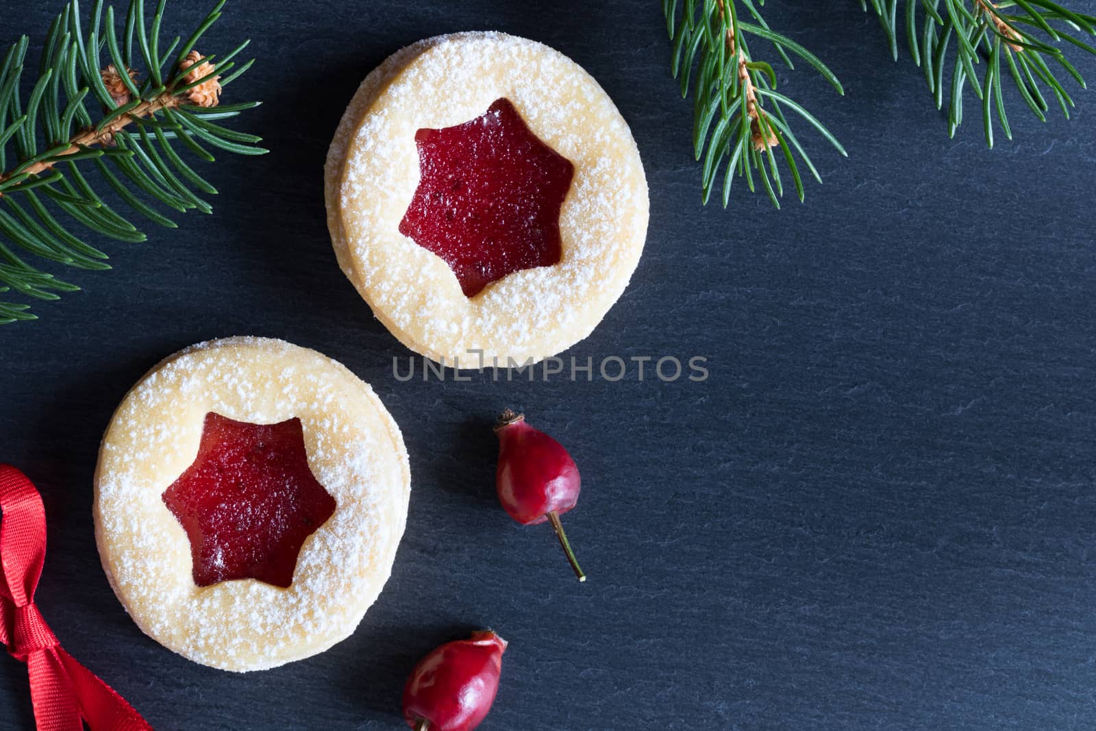 Dark Christmas background with two Linzer Christmas cookies, dried rose hips and spruce branches