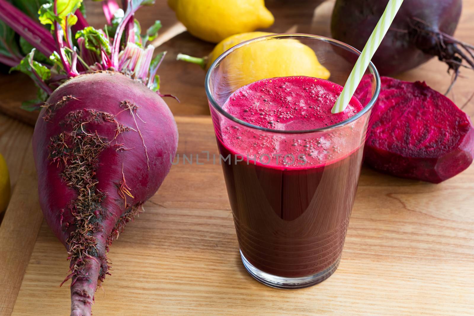 Red beet juice in a glass on a wooden background with lemon and whole beets
