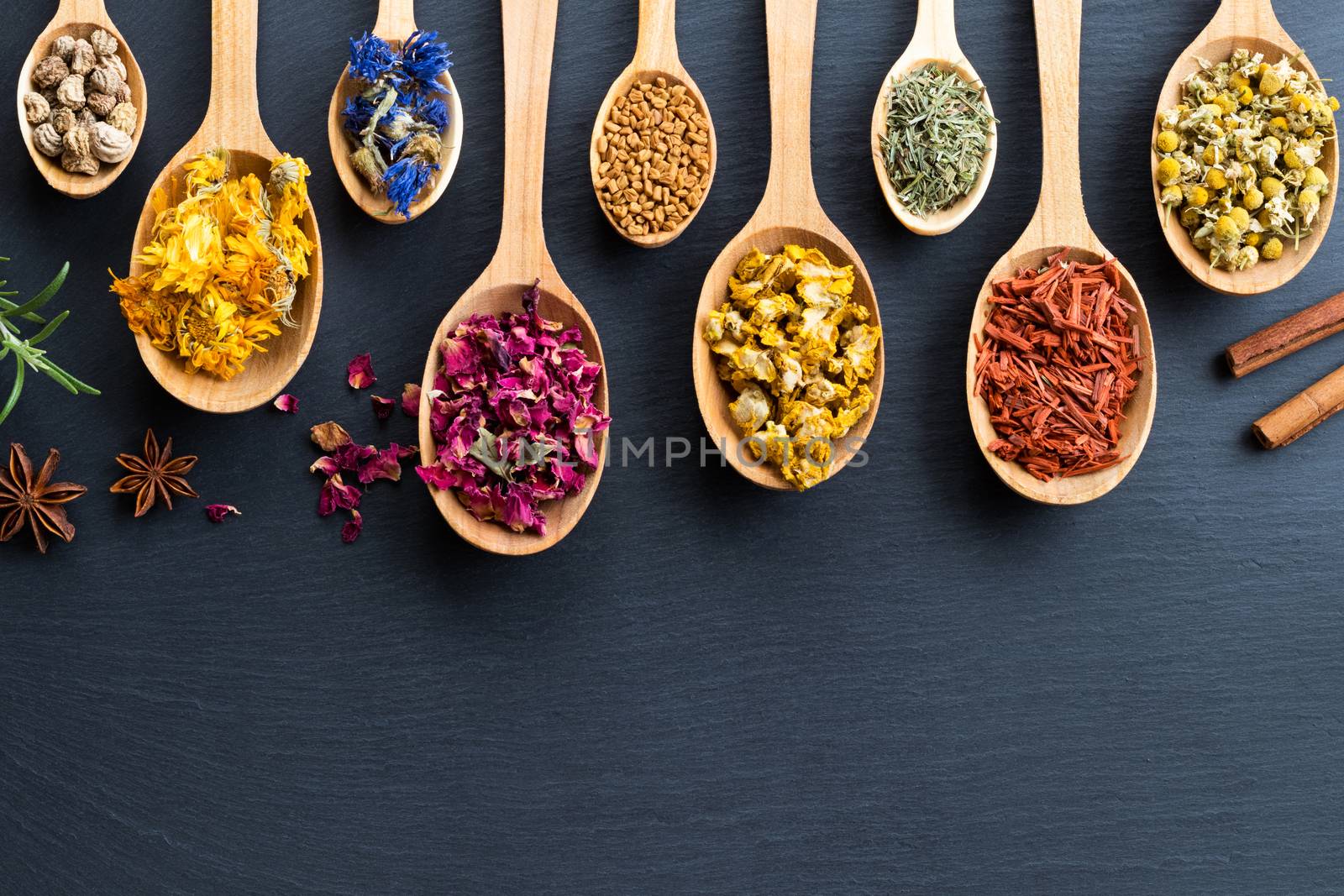 Herbs on spoons on a wooden background with copy space, top view. Nasturtium seeds, calendula, cornflower, rose petals, fenugreek seeds, mullein, horsetail, sandalwood, chamomile.