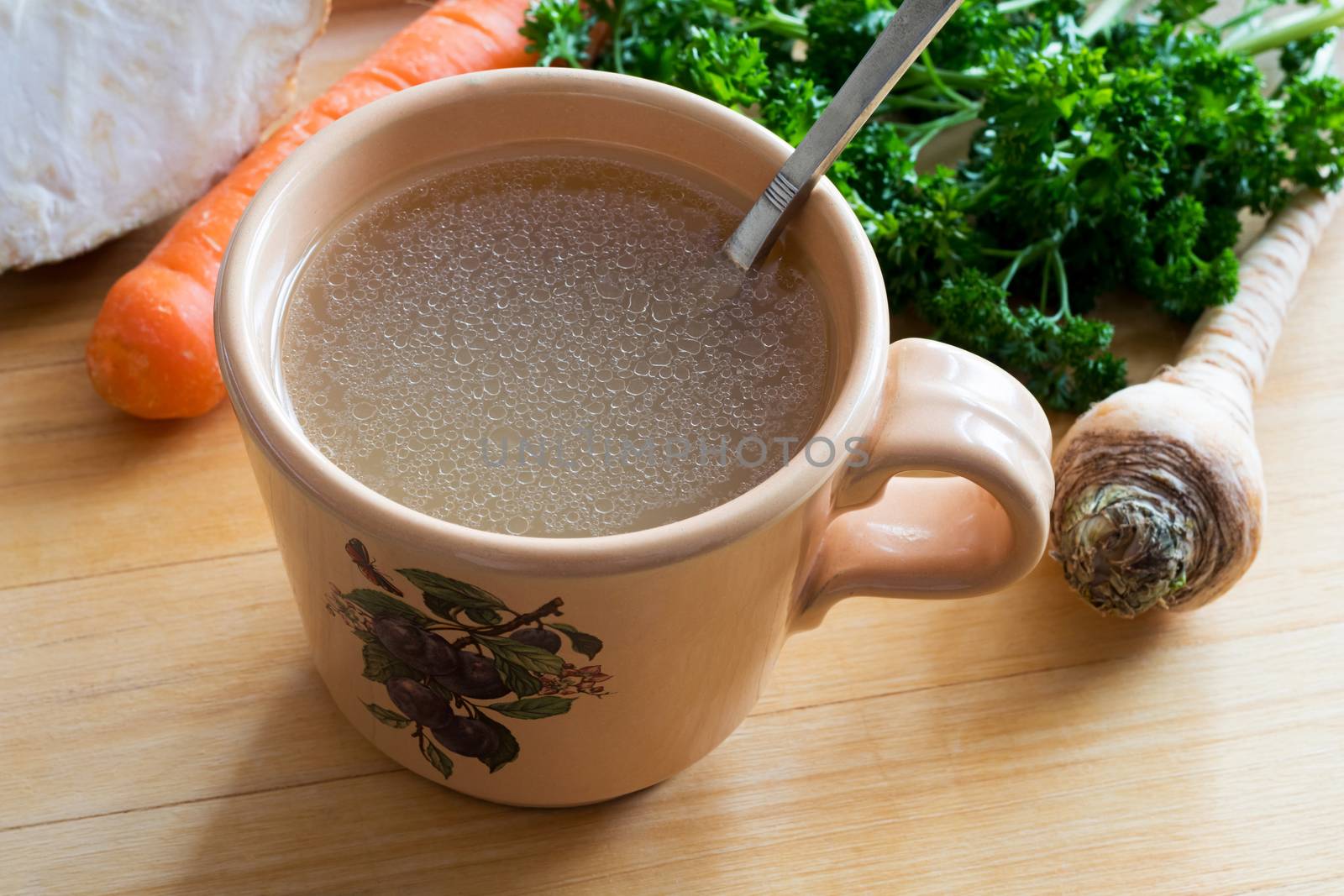 Chicken bone broth in a mug with fresh vegetables in the background
