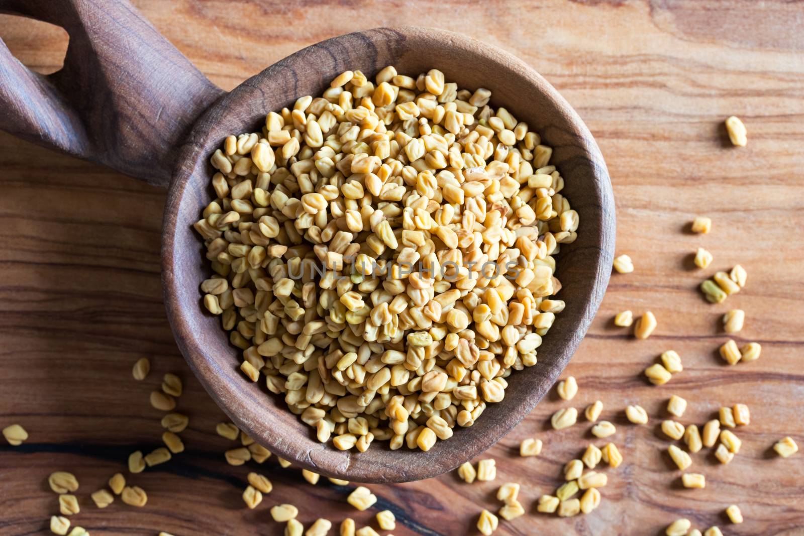 Fenugreek seeds on a wooden spoon, top view.