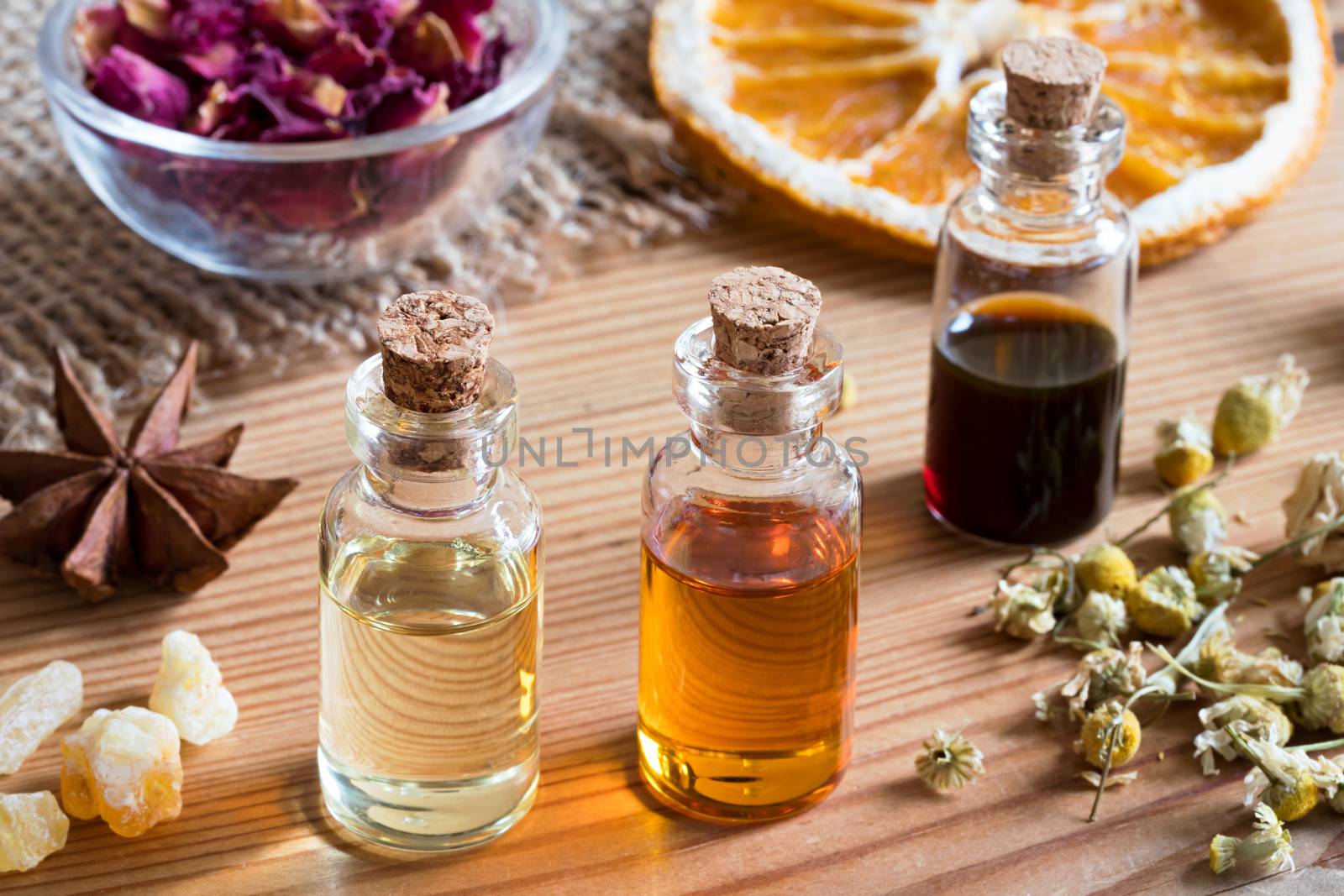 Bottles of essential oil with dried chamomile flowers, orange slices, frankincense and star anise on a wooden table
