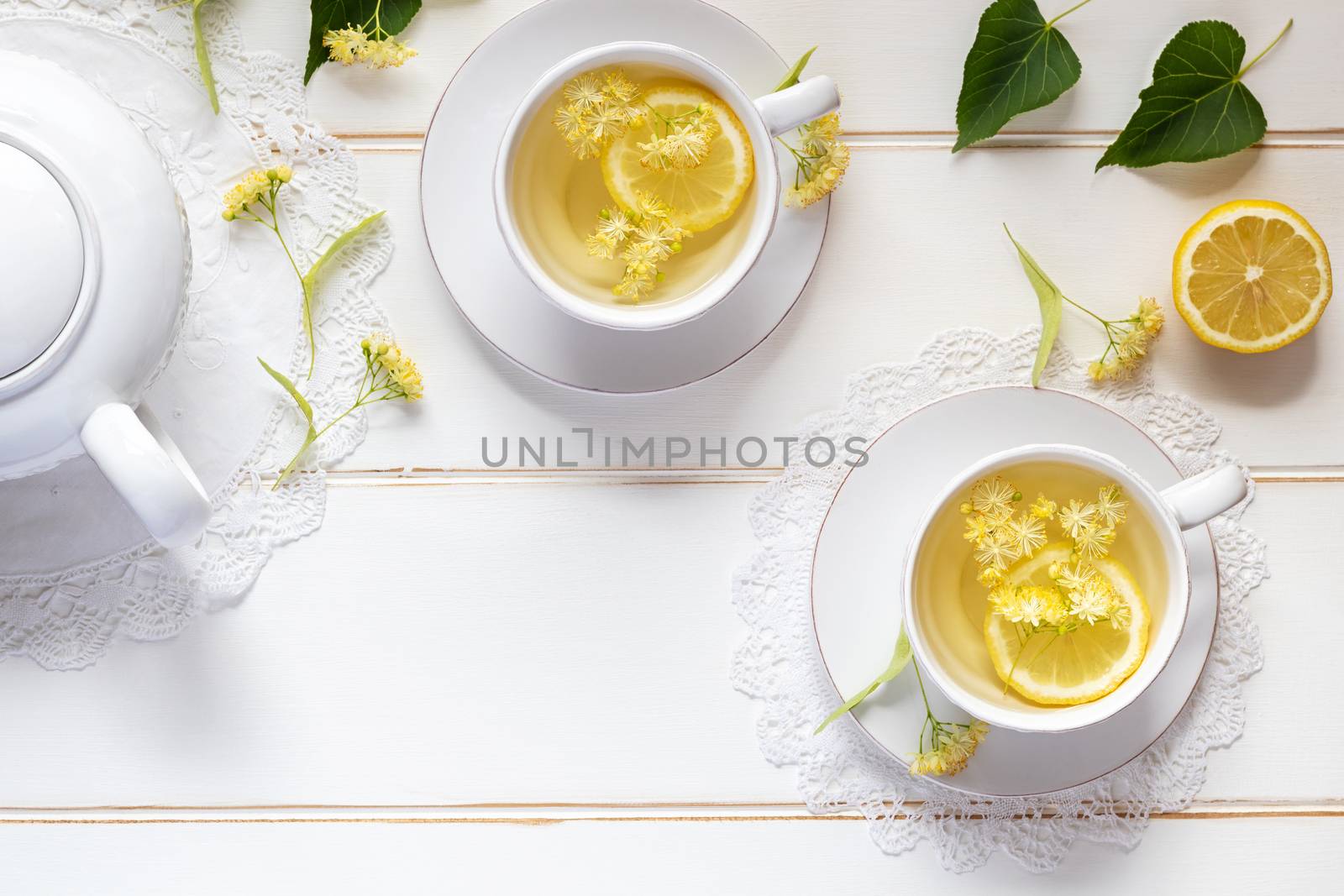 Two cups of herbal tea with linden flowers and lemon on a white table, with copy space