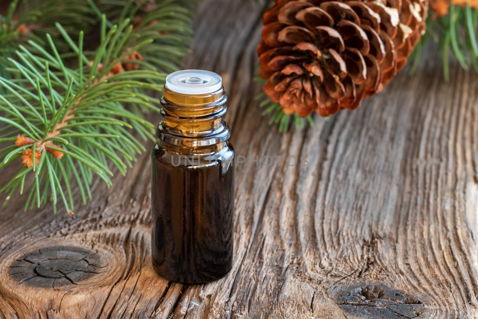 A bottle of essential oil with spruce branches on a rustic background