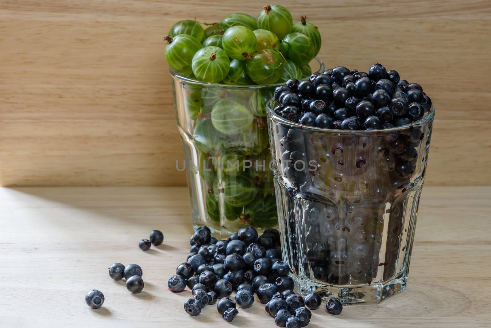 Blueberries and gooseberries in a glass with scattered berries. Good addition for breakfast