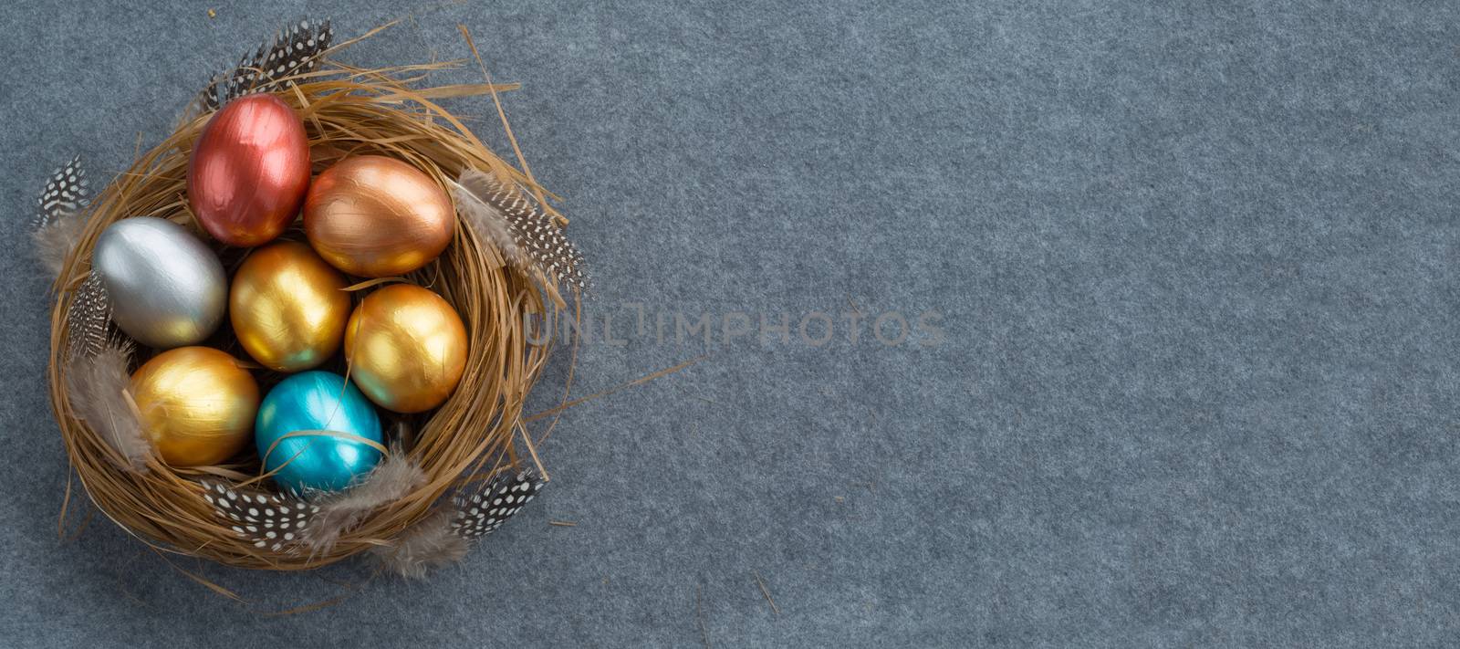 Happy Easter holiday greeting symbol stylish natural wooden grass nest with colorful quail eggs and feathers on gray fabric background with copy space for text