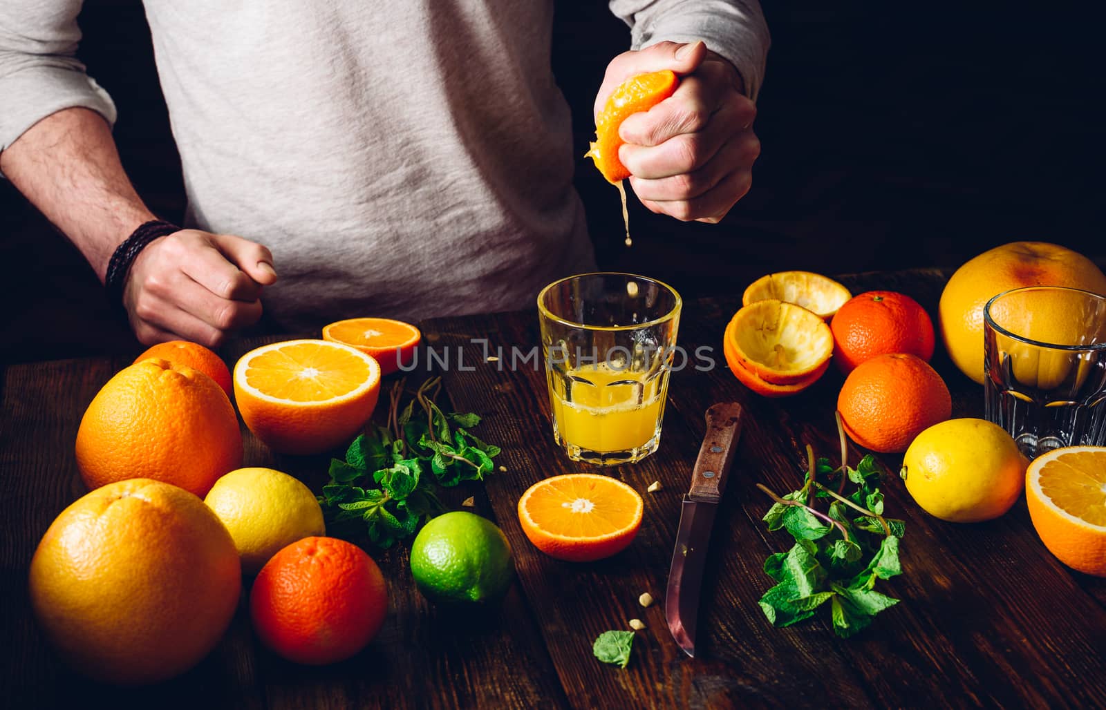 Guy Squeezes the Citrus Juice. Glass of Juice, Fruits and Mint on Table.