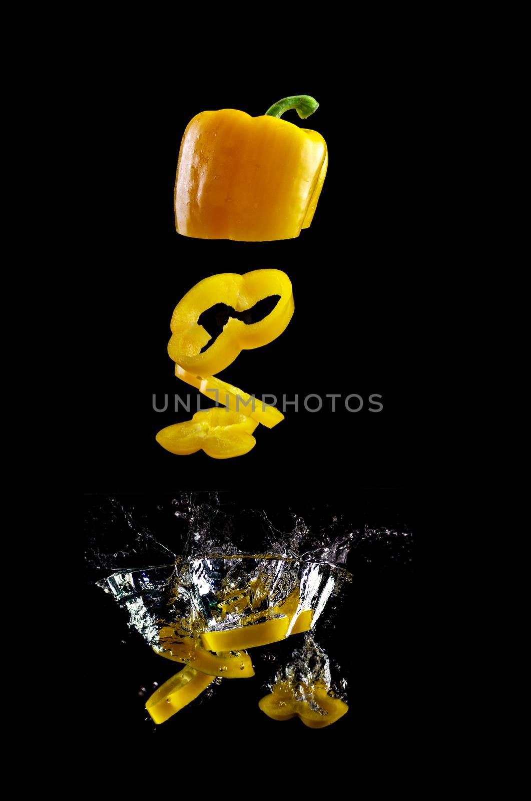 Tomato, two types of paprika and eggplant slices fall into water, on black background