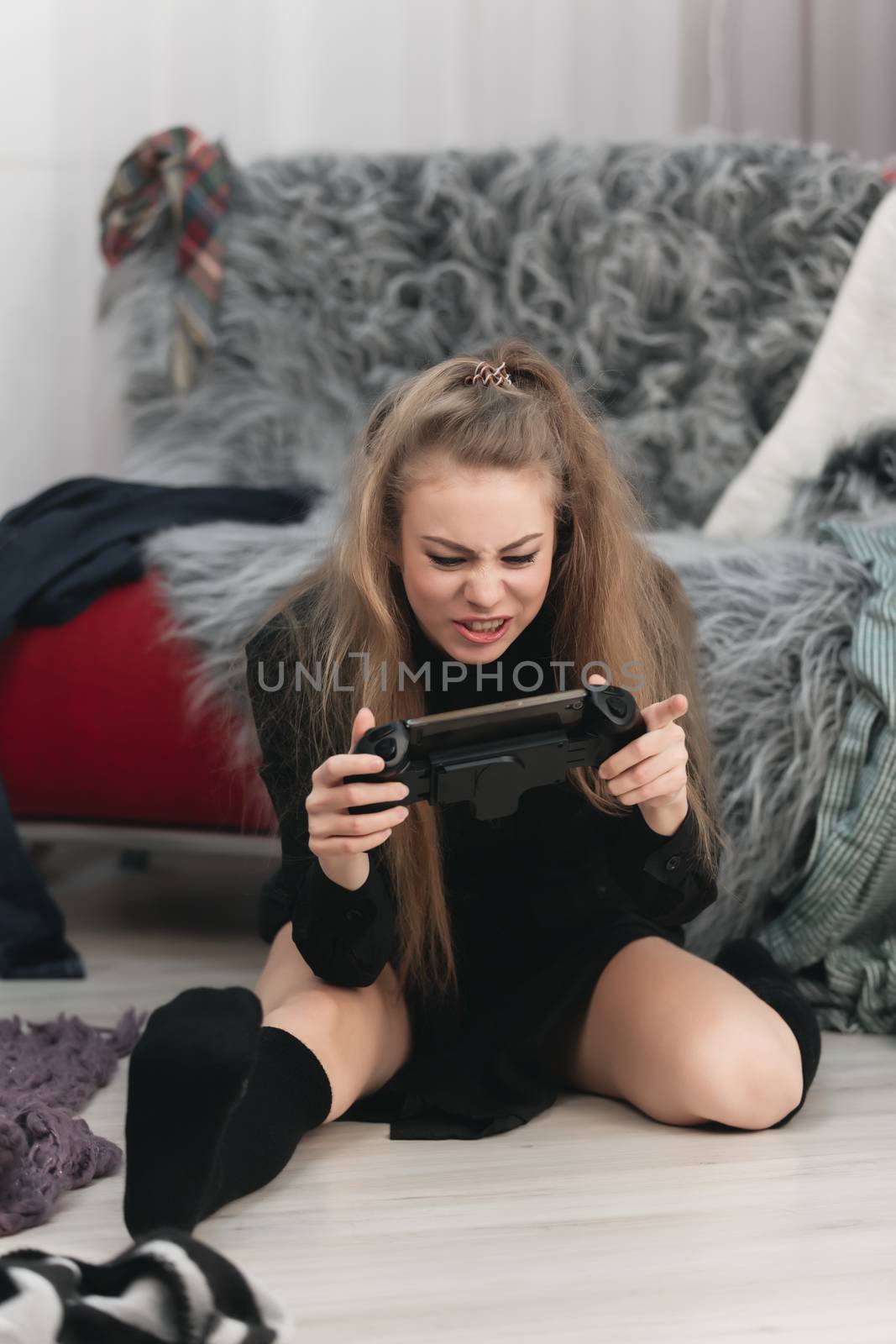 girl woman gamer playing on the phone with a gamepad sitting on the floor, around the mess