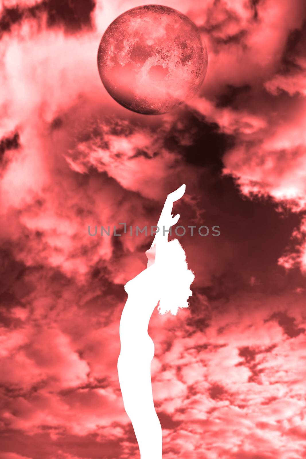 attractive silhouetted nude woman holding her hands up to the sky giving gratitude to the blood red moon in a yoga pose with a cloudy background