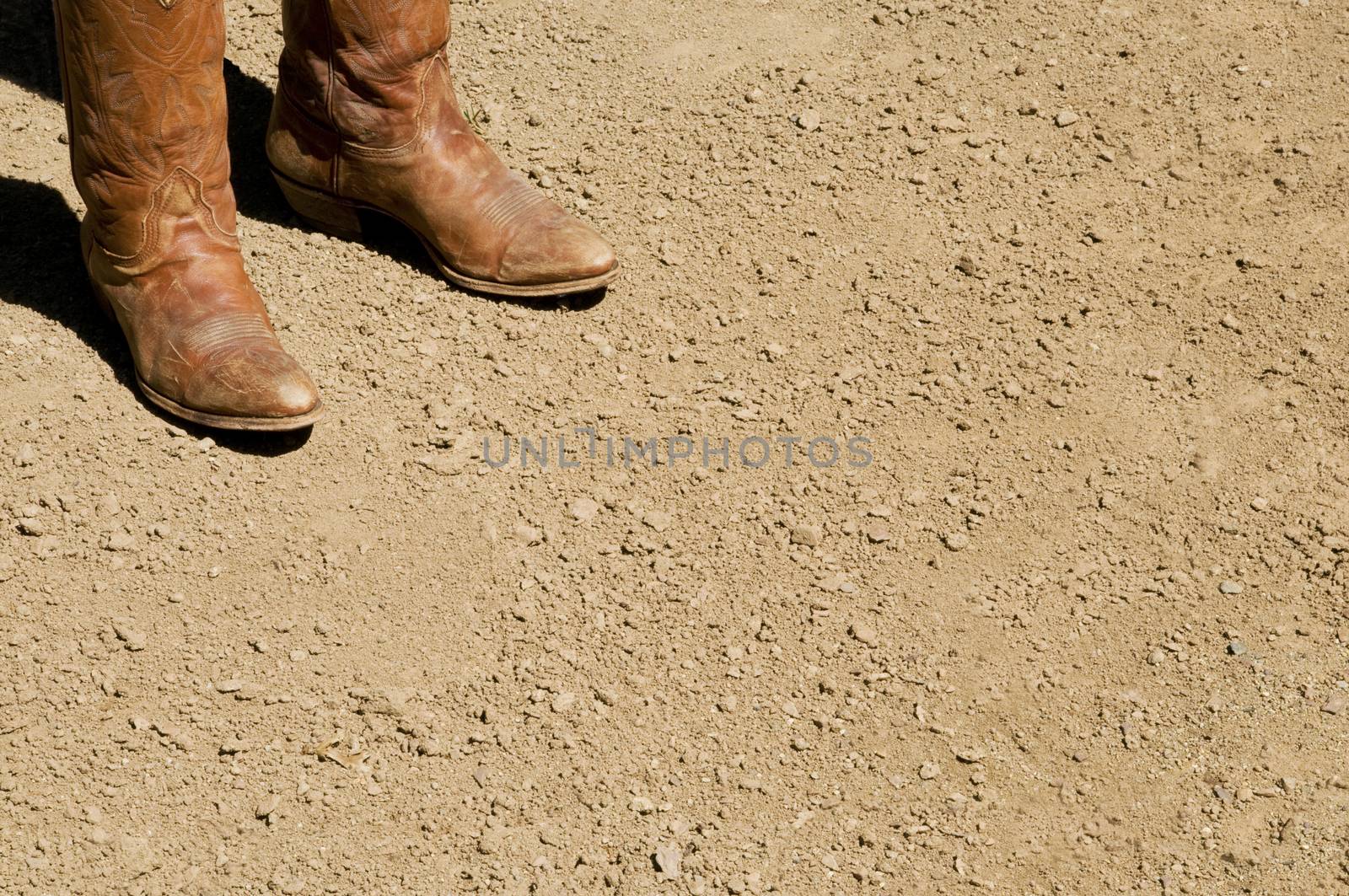 Two dirty western cowboy boots standing on dry dirt ground