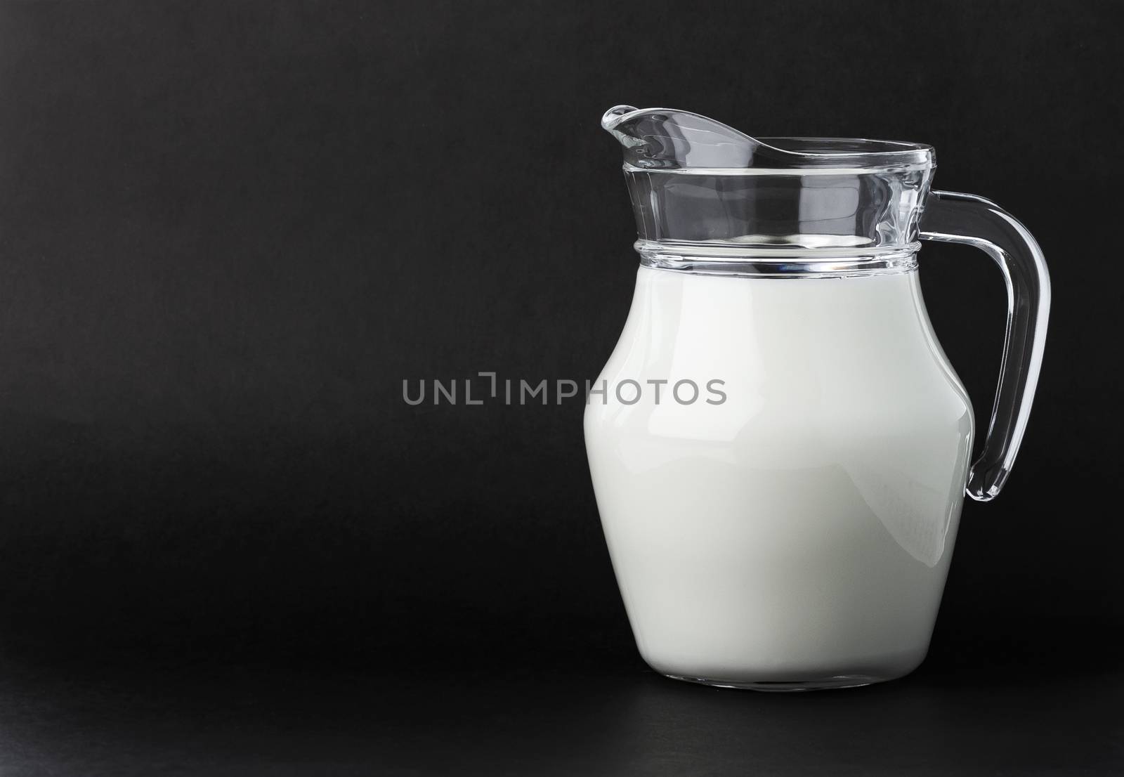 Glass jug of fresh milk on black background with copy space, pitcher of cream