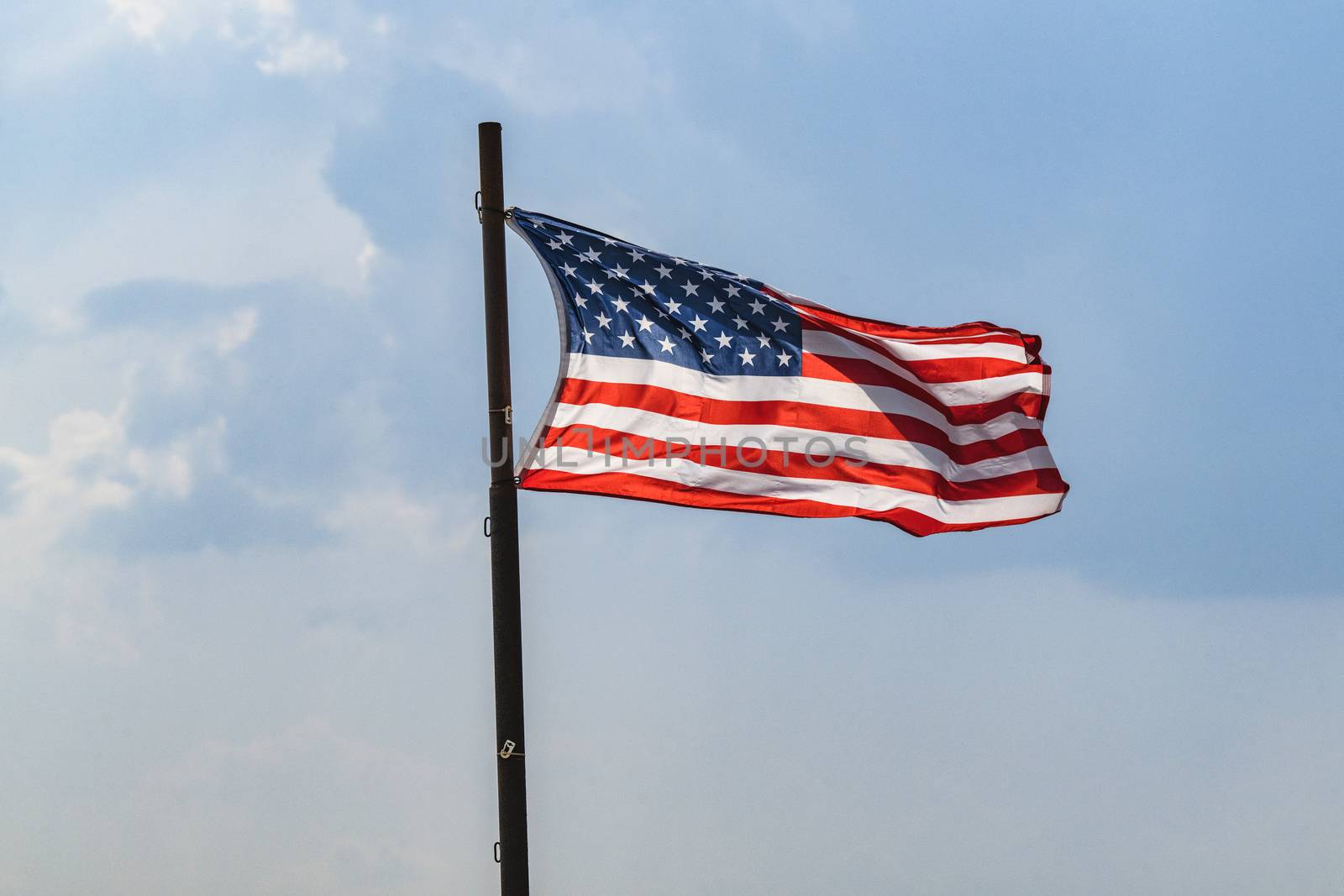 The flag of USA on a flagpole waving in the wind on a blue sky