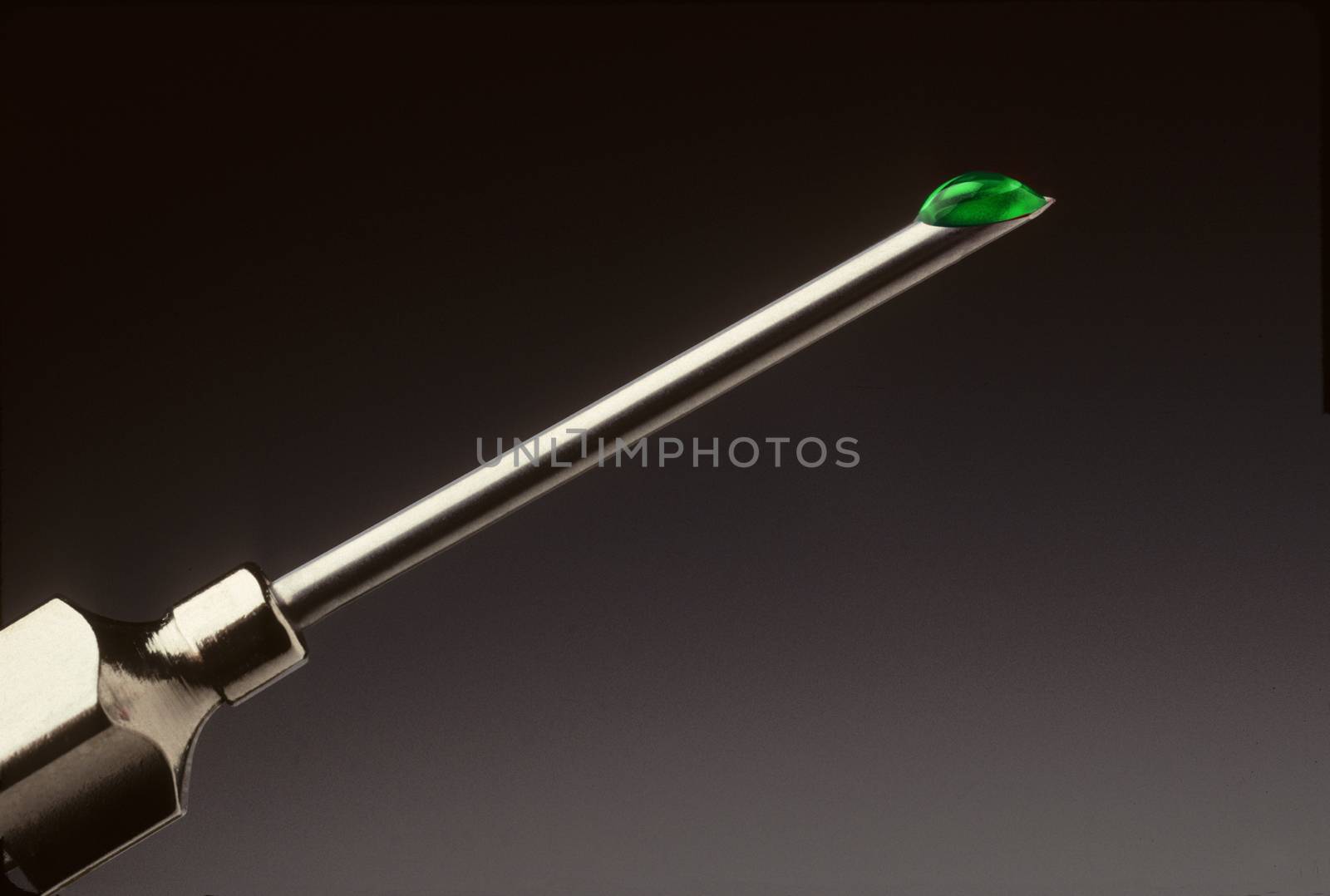 Closeup of a drop of green liquid at the tip of a hypodermic needle
