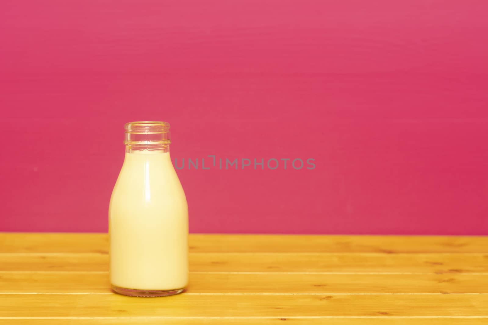 Banana milkshake in a one-third pint glass milk bottle, on a wooden table against a pink painted background
