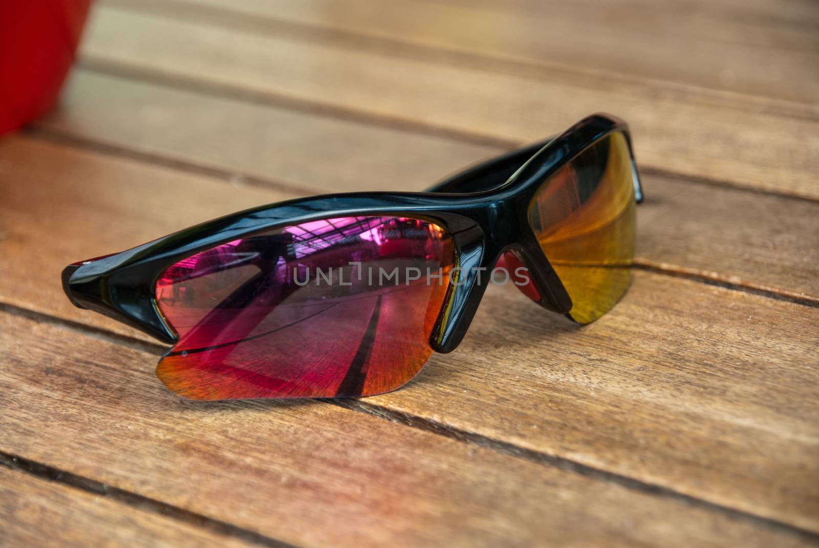Red to yellow gradient sun glasses lying on wood table outside