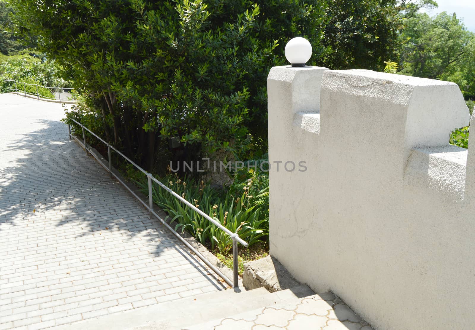 Walking path with steps in the Park, along a beautiful stone fence with white plafonds, in summer.