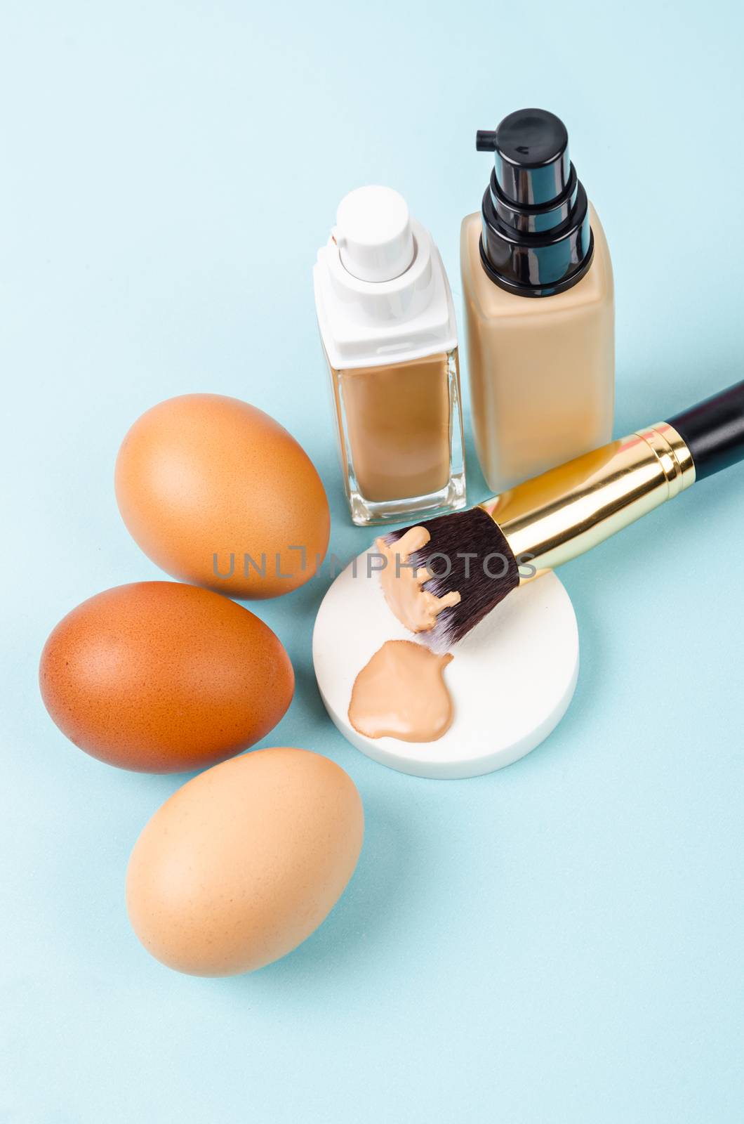 Liquid fluid foundation glass bottle on makeup sponges and egg on pink background. Choose tone color foundation makeup for skin concept.