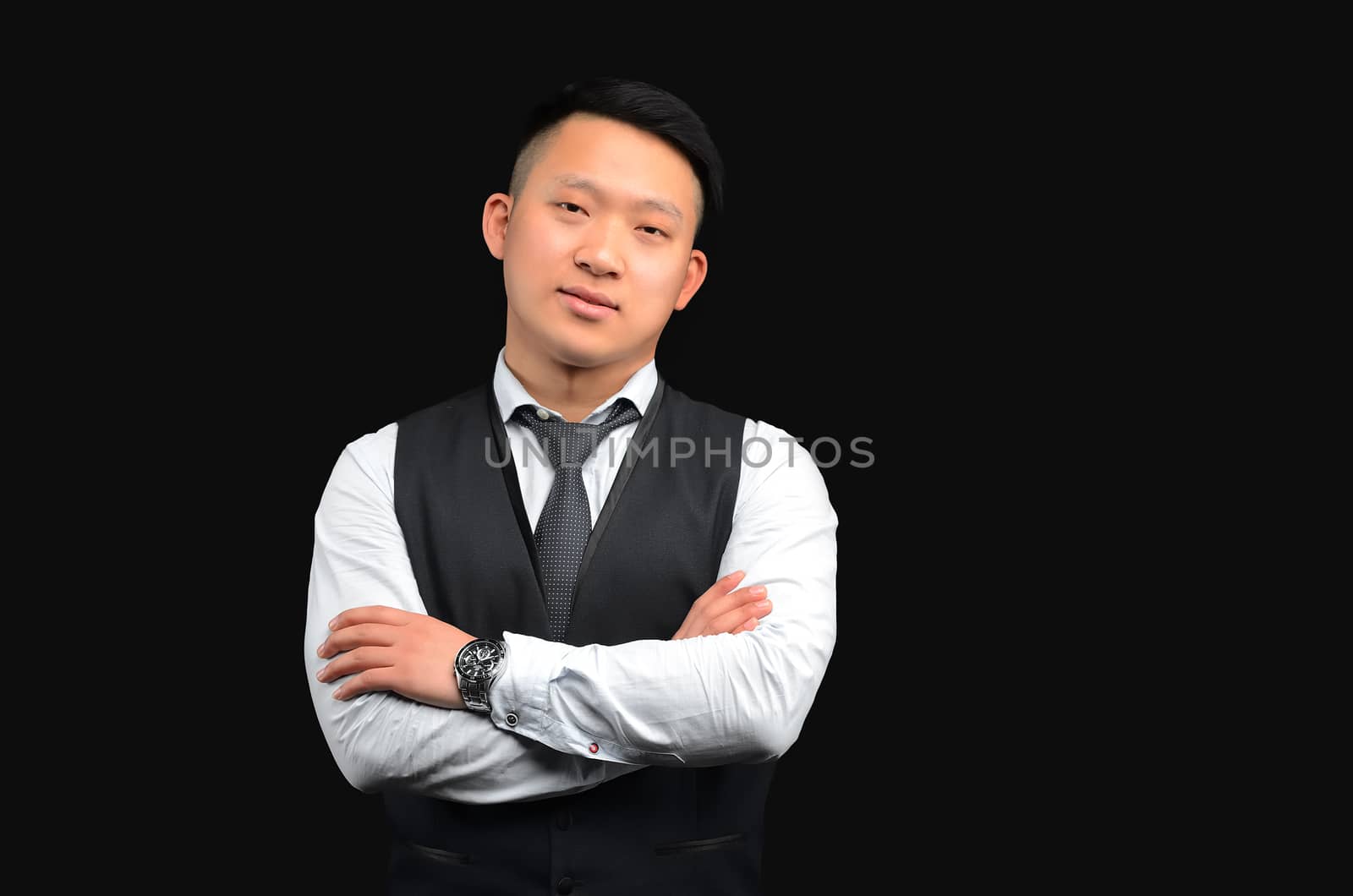 Asian young man stands on a black background, looks at the camera, crosses his hands