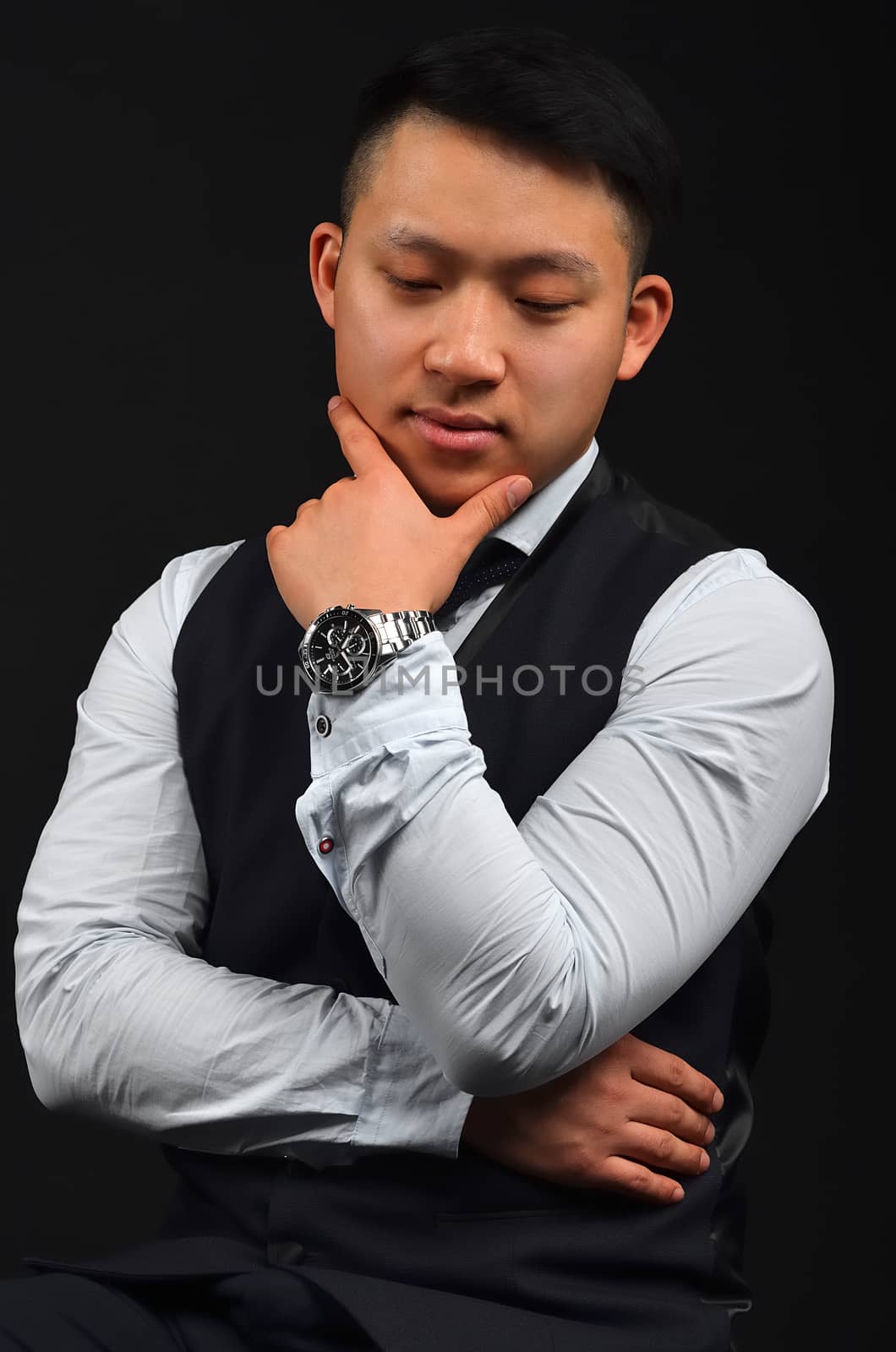 A thoughtful young Asian man has put a hand with a clock to face, looks down