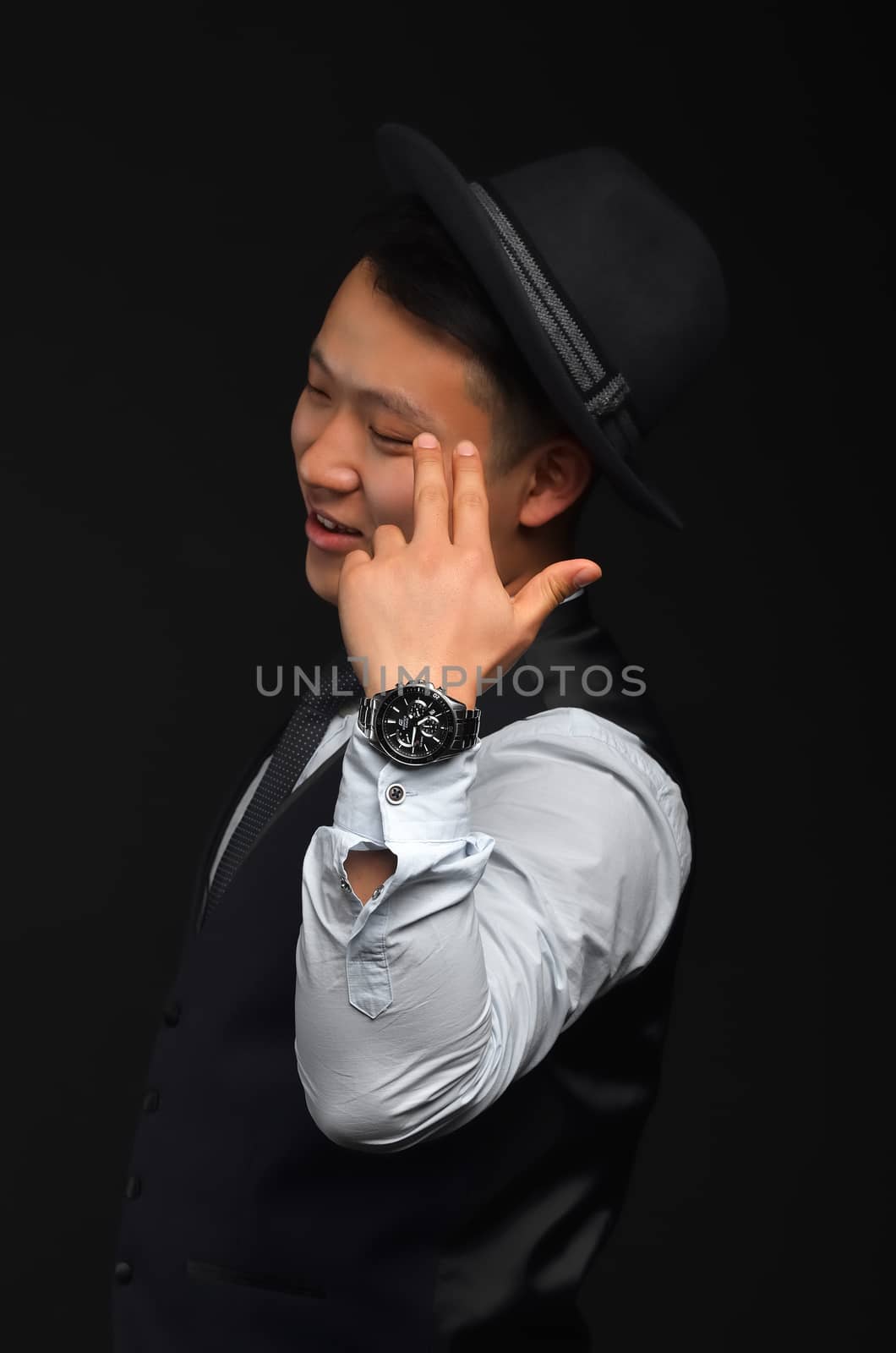 A young Asian man in a black hat, closed his eyes and put his fingers against his head like a pistol