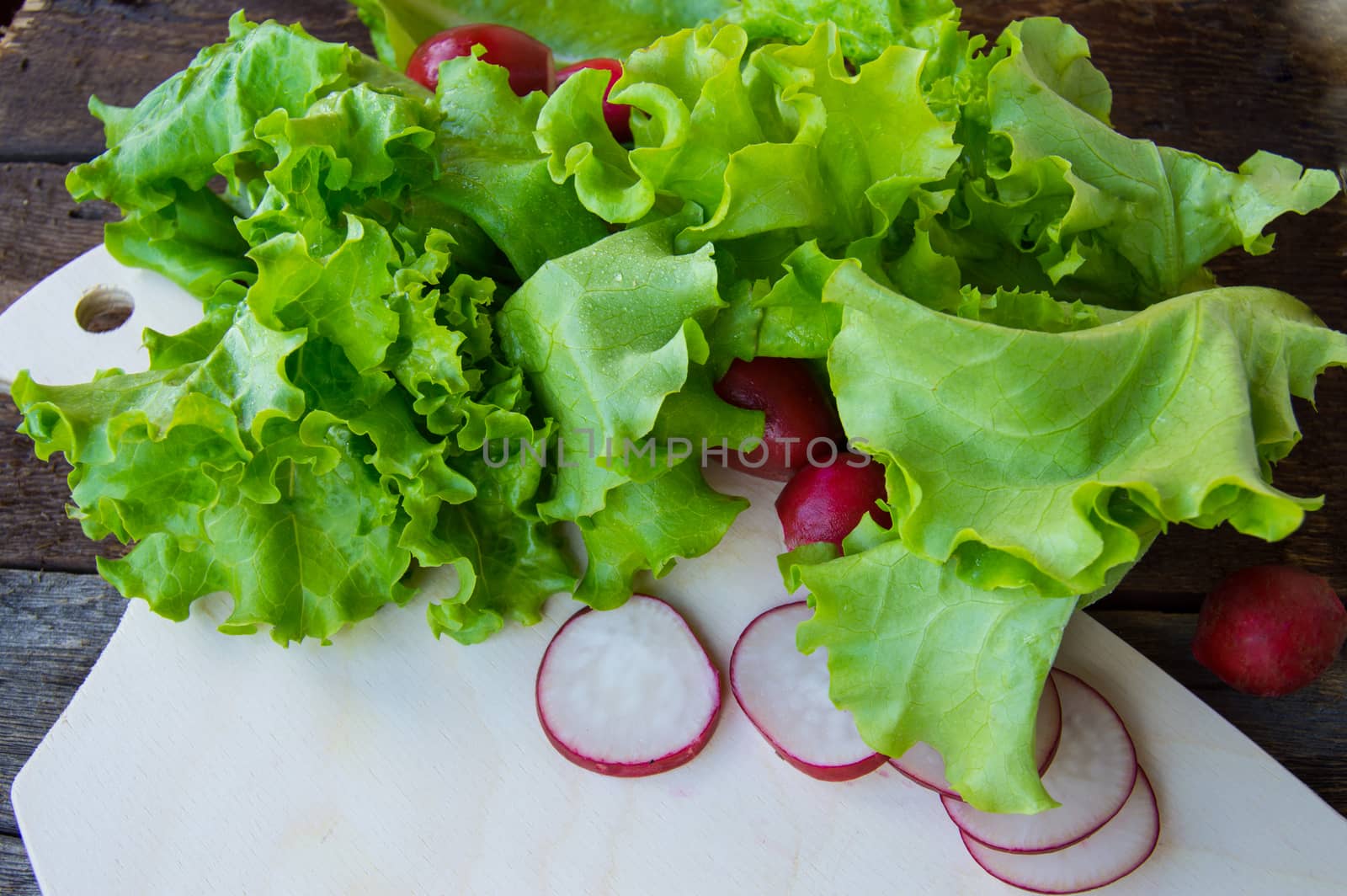 Radishes and fresh organic lettuce on a dark wooden background by claire_lucia